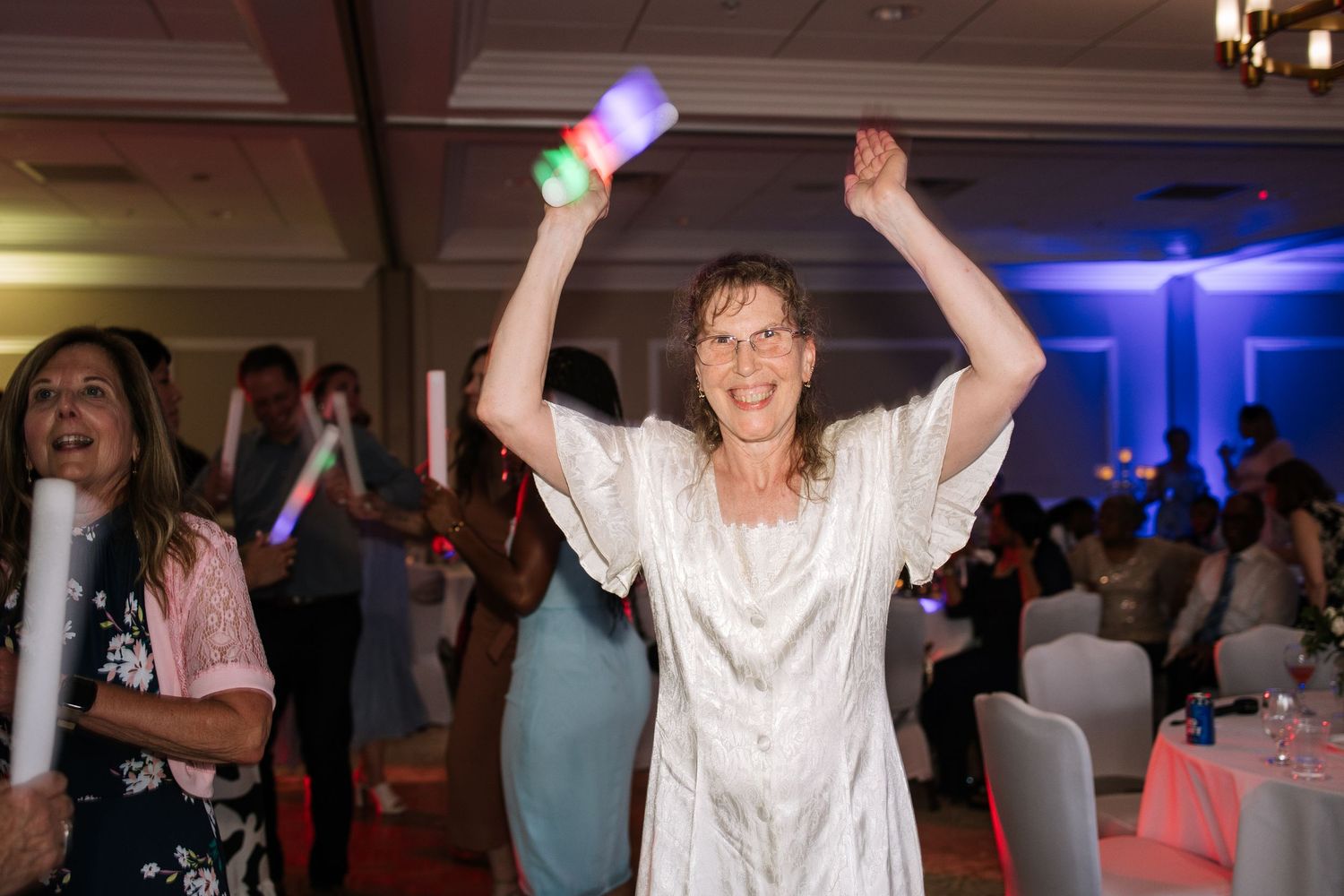People dancing and celebrating at a reception with purple and blue lighting effects.