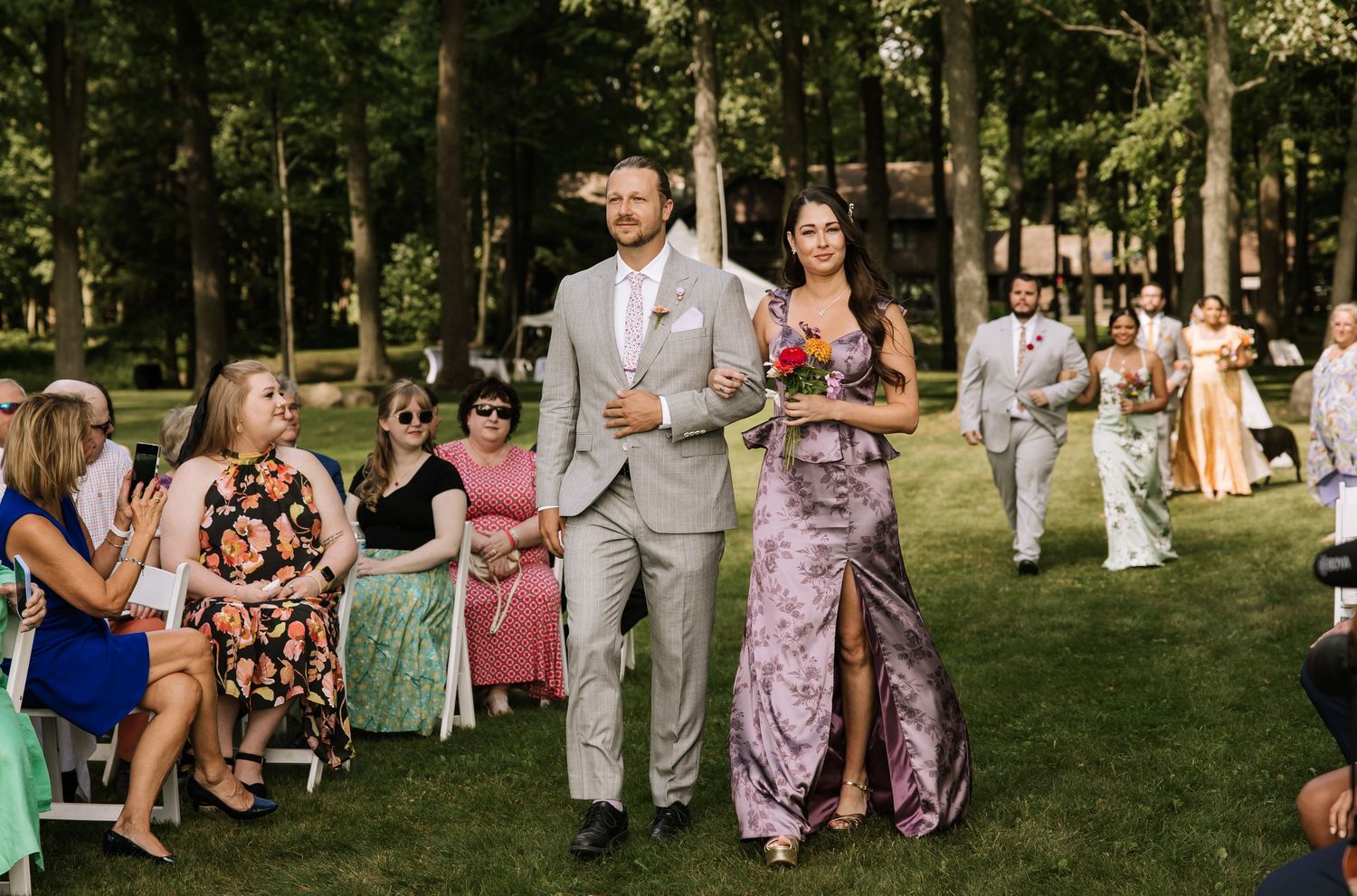 Wedding party and guests gathered outdoors on a green lawn during a summer celebration.