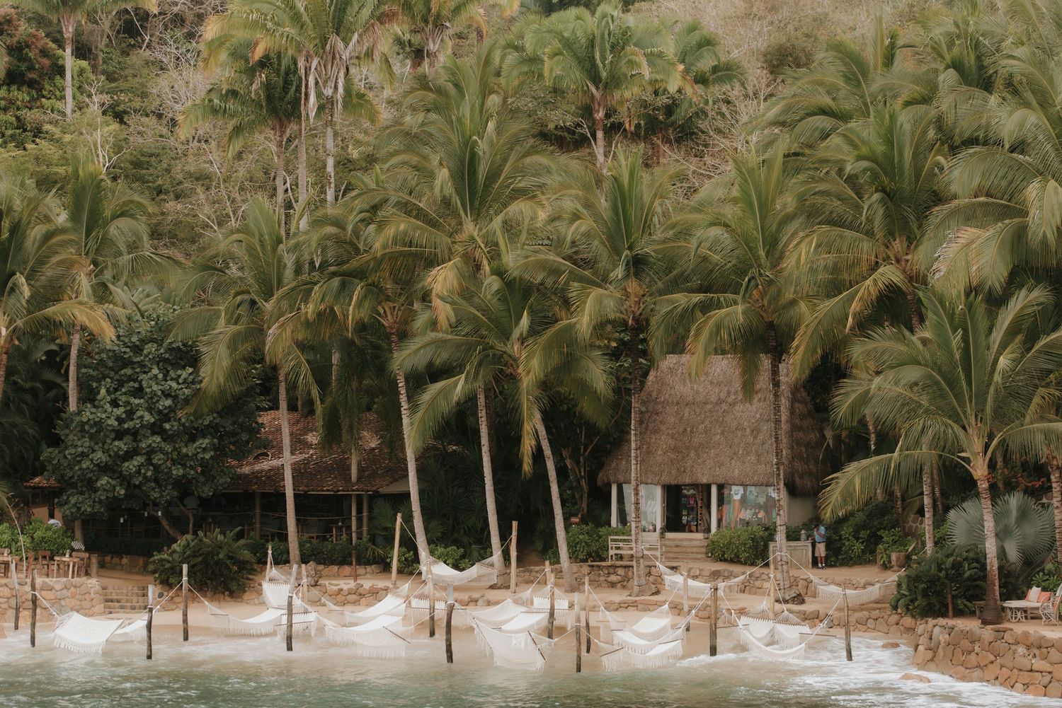 Tropical beach resort with thatched-roof hut and palm trees along the shoreline.