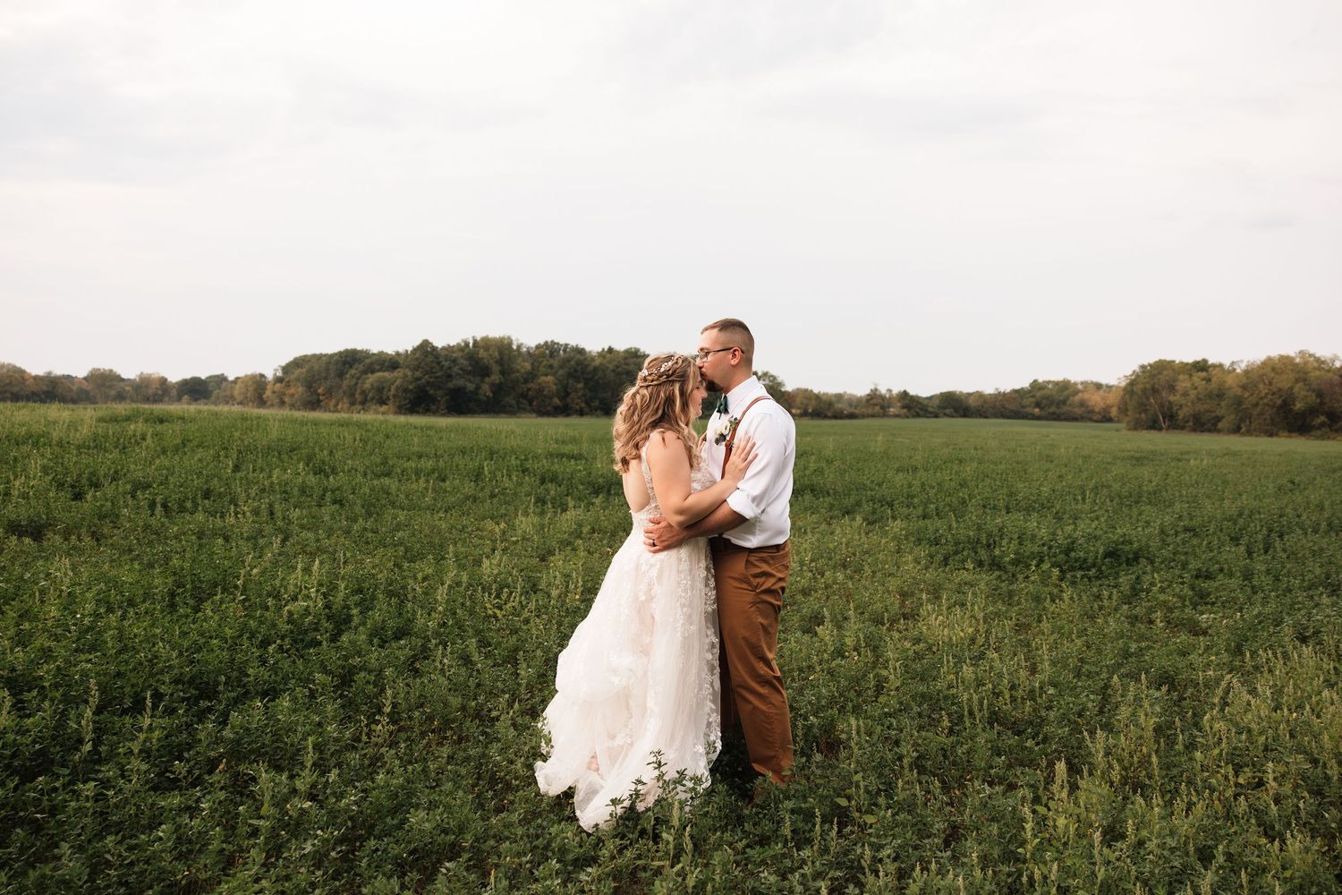 Wedding couple embracing in a lush green meadow at dusk.