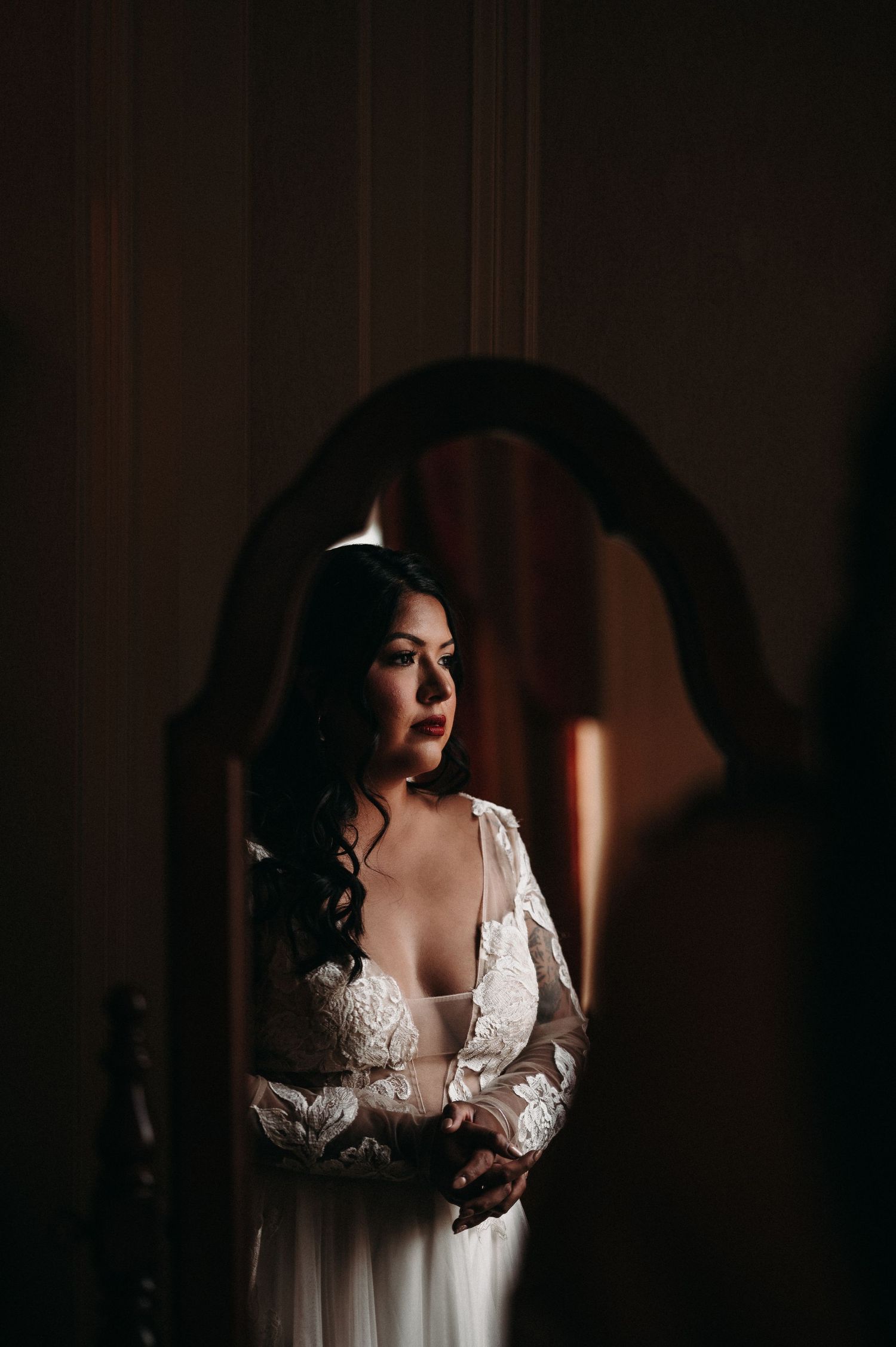 Artistic bridal portrait through an arched frame with dramatic lighting and a lace dress.