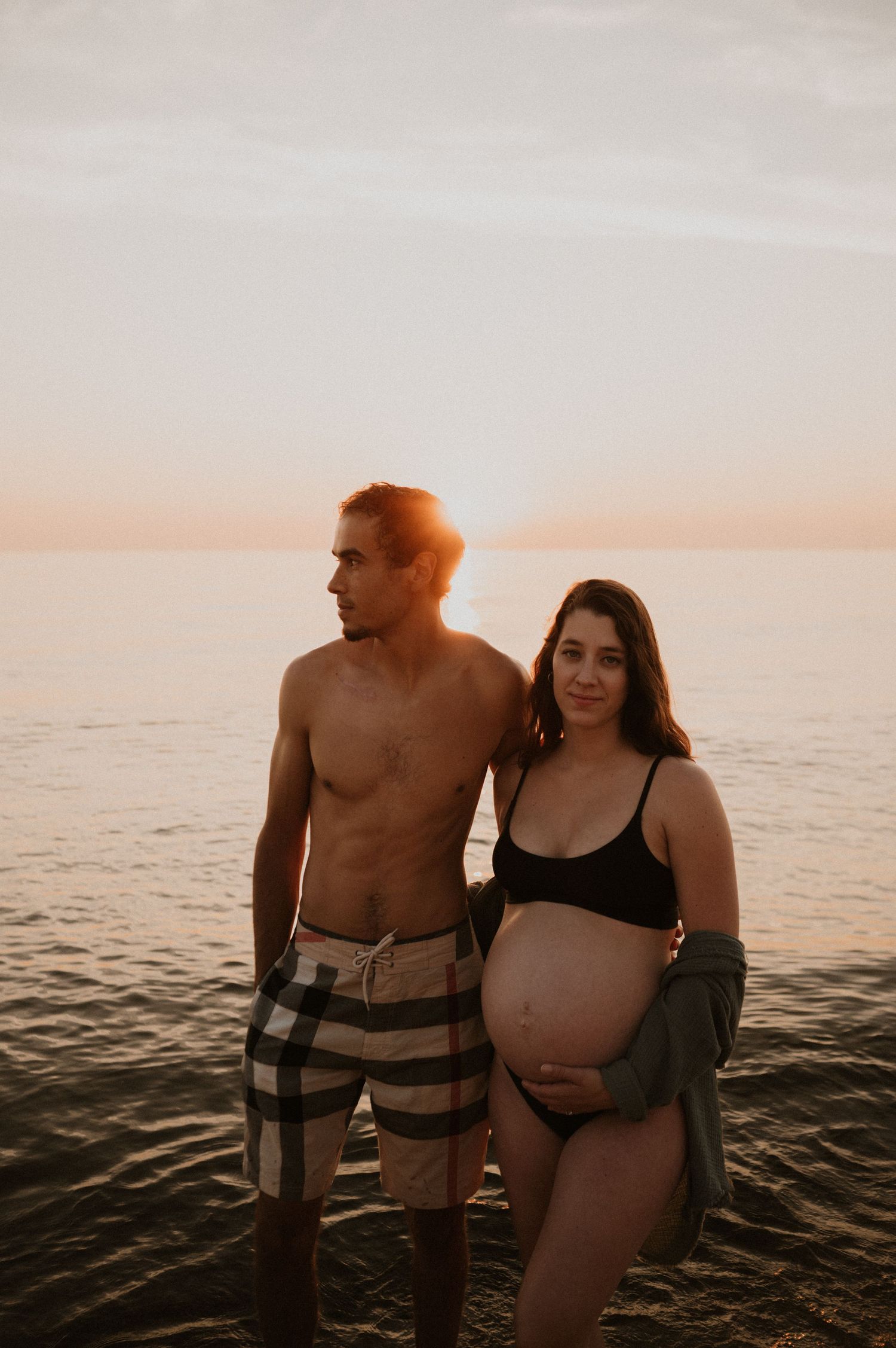 Maternity beach portrait with couple standing together at golden hour.