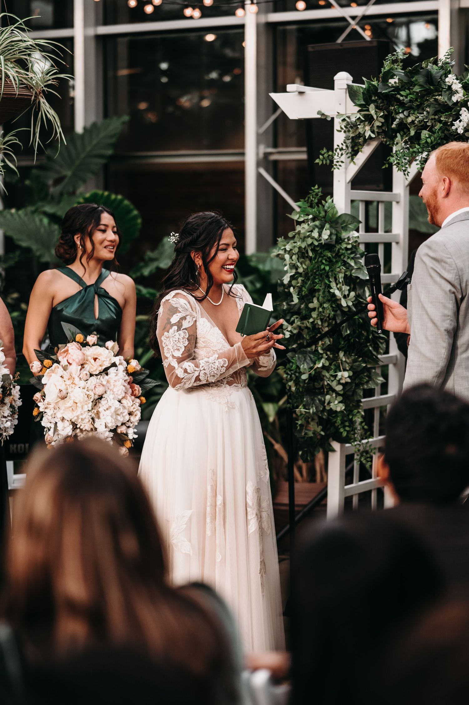 Emotional moment during vow exchange at greenhouse wedding with bridesmaids and guests looking on.