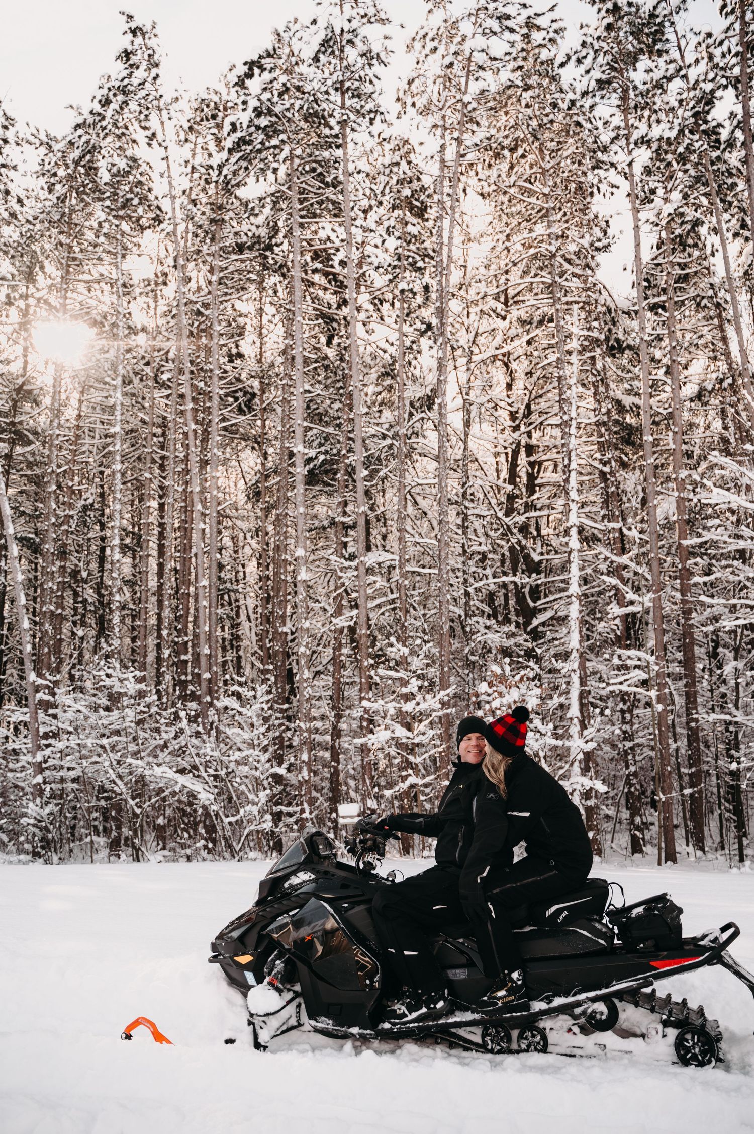 Snowmobile rider navigating through a winter forest with sunlight filtering through snow-covered trees.