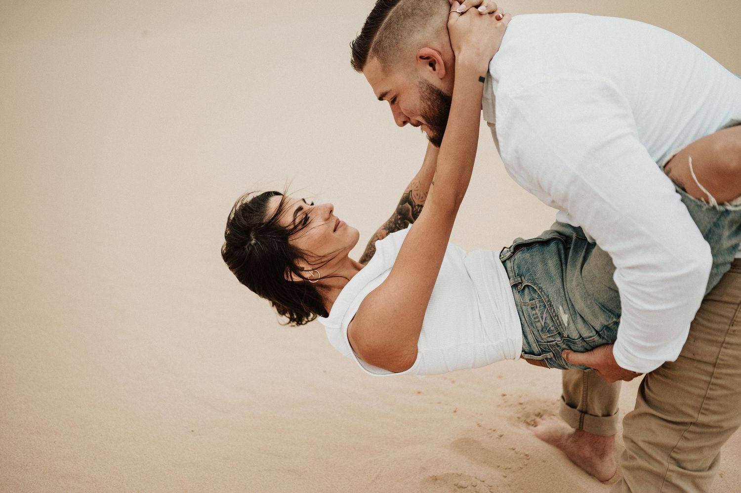 A couple plays and laughs together on sandy dunes during an intimate photoshoot.