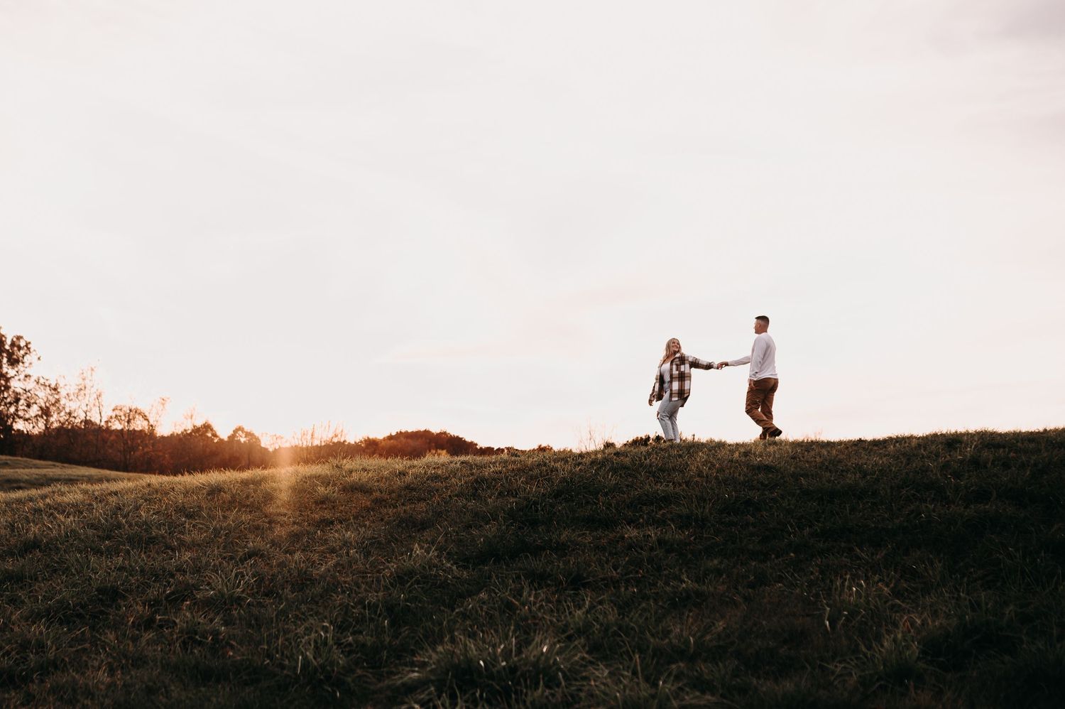 Silhouettes of couple dancing together on hilltop at sunset.