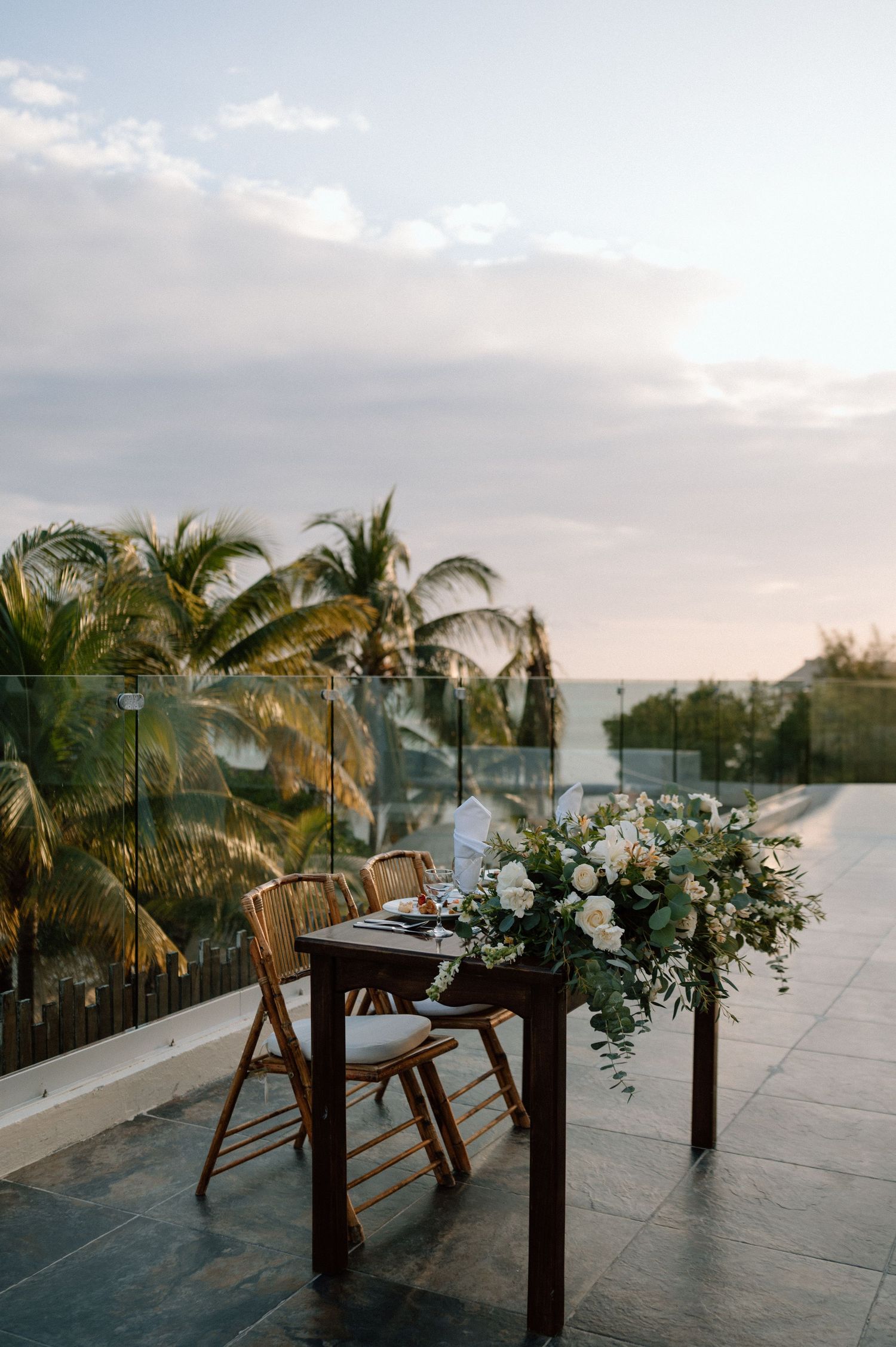Tropical wedding reception setup with palm trees and decorated tables at sunset.