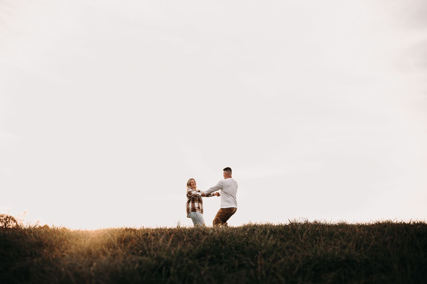 Silhouettes of couple dancing together on hilltop at sunset.