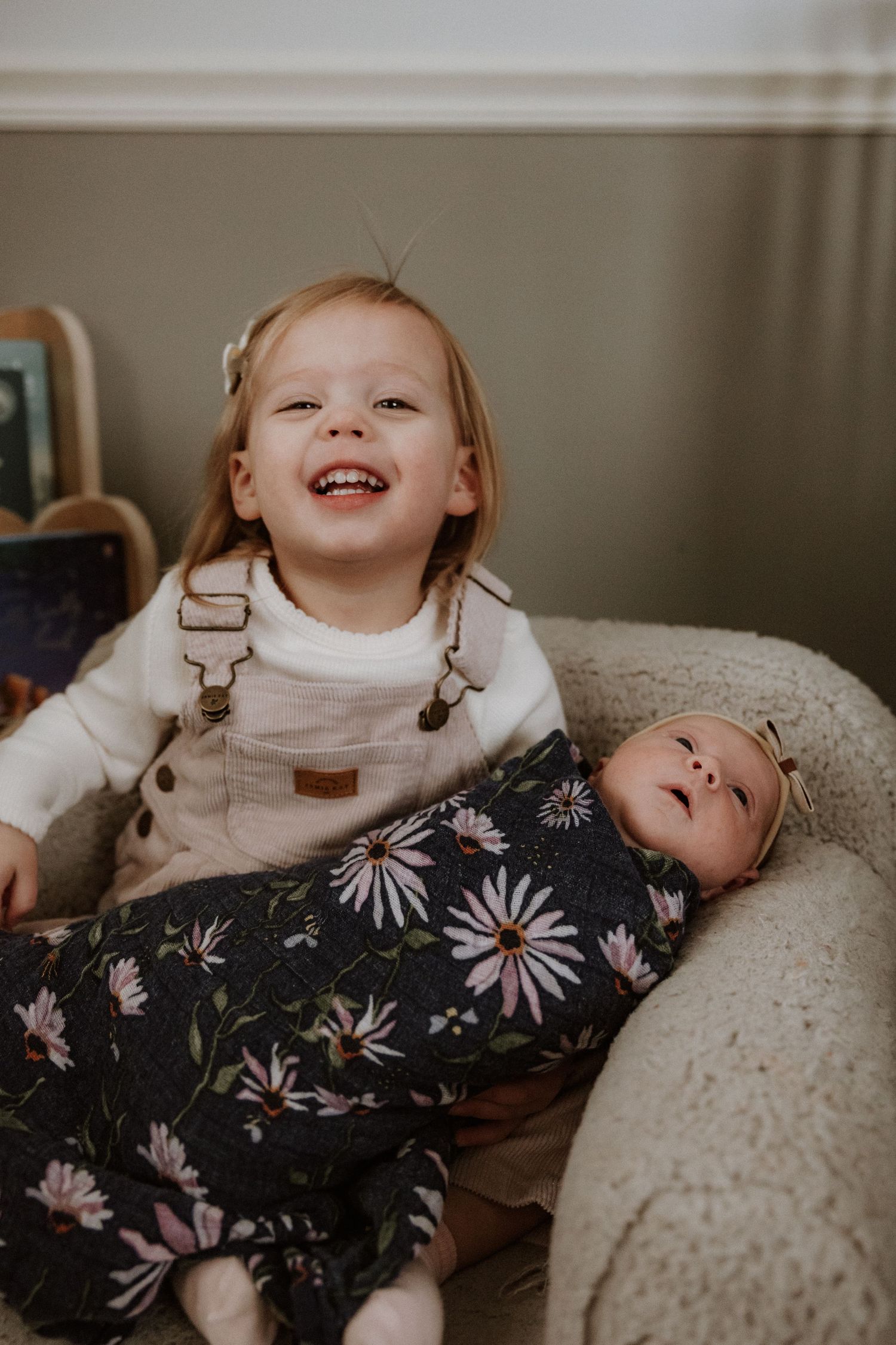 Toddler and baby resting on a plush beige couch with floral print clothing.