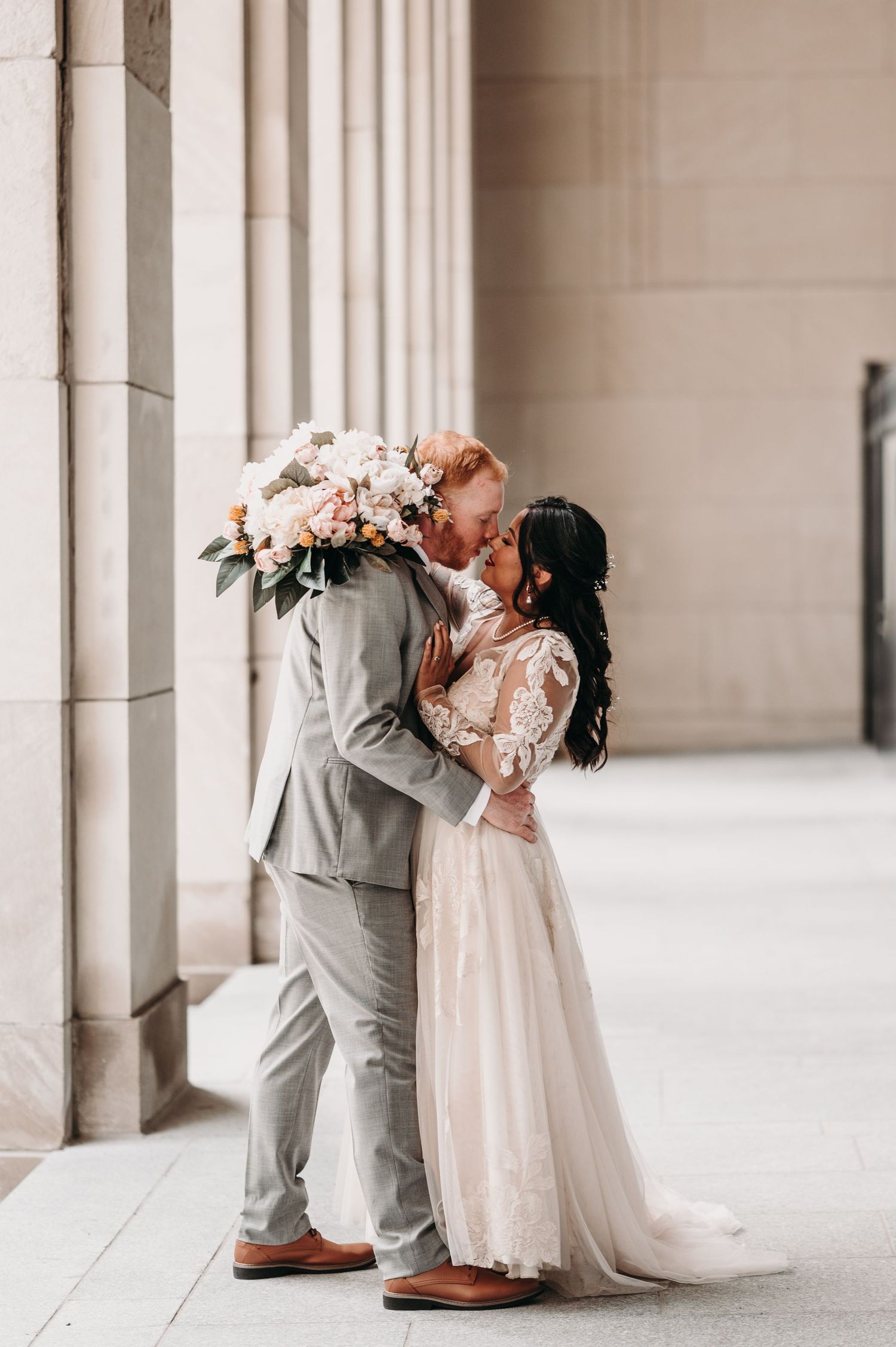 A romantic wedding moment captured between newlyweds in front of classic stone columns.