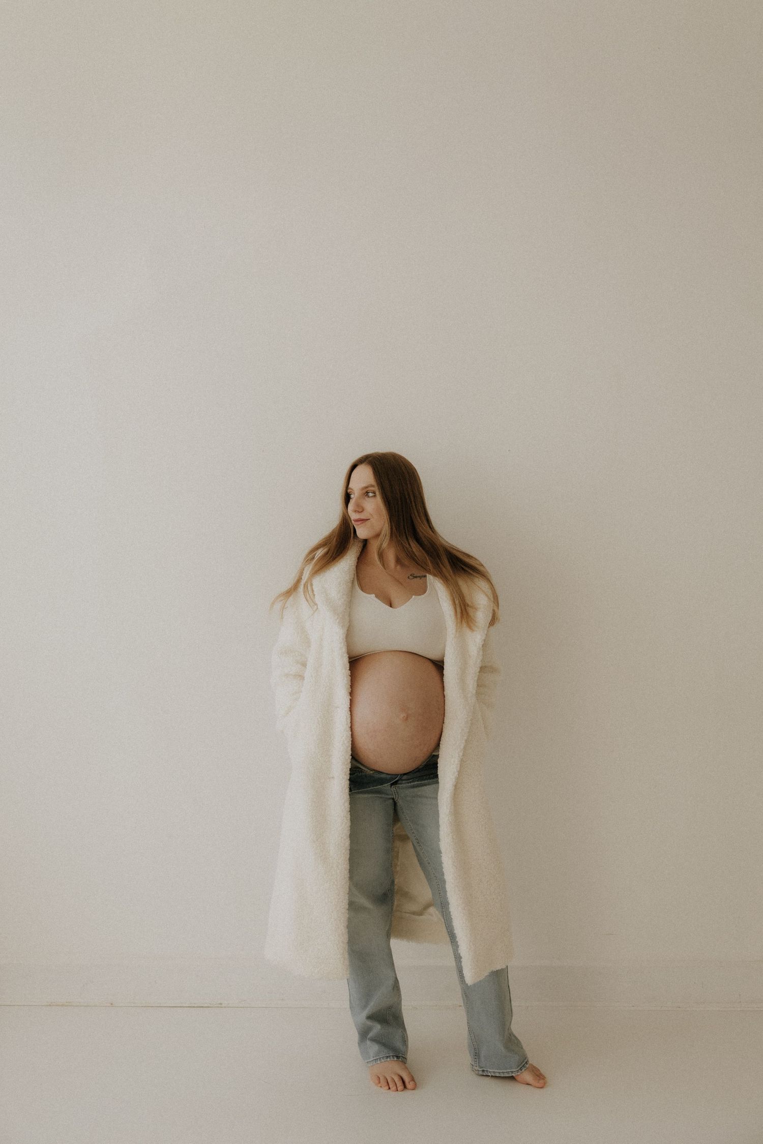 Artistic maternity photos showing expectant mother in white crop top and jeans.