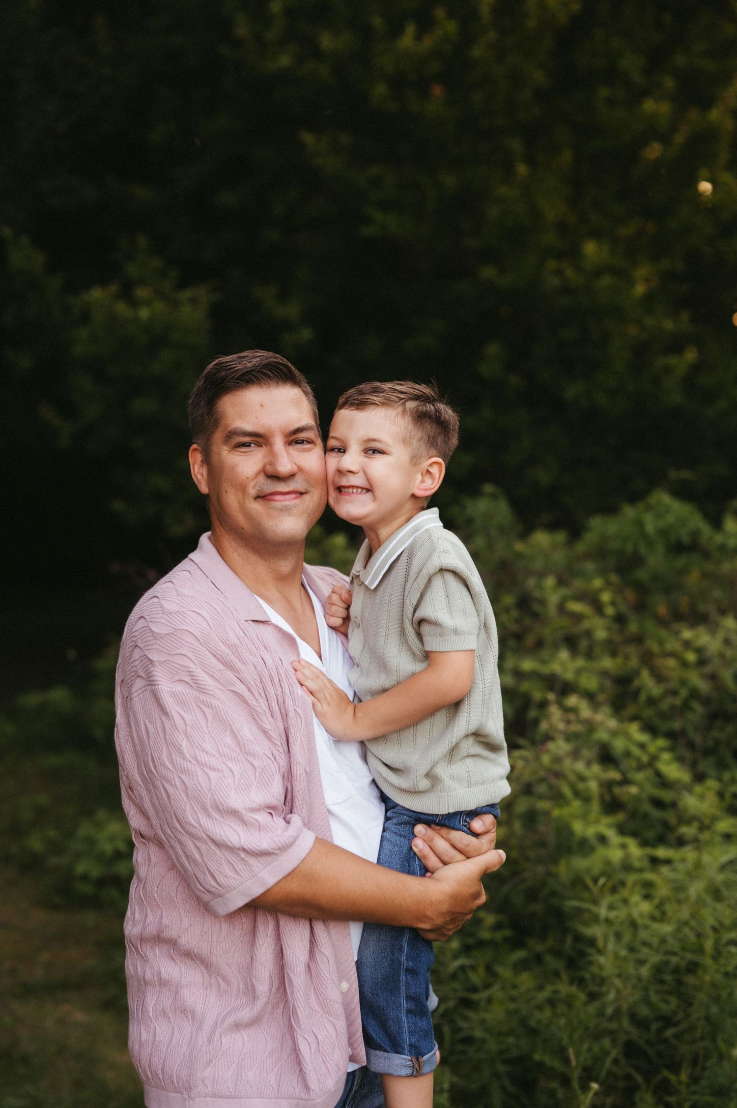 A heartwarming outdoor portrait featuring two people against green foliage.