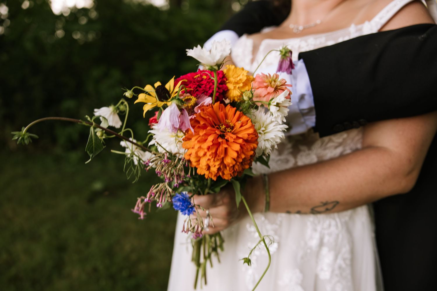 Vibrant orange and wildflower wedding bouquet held against a white dress.