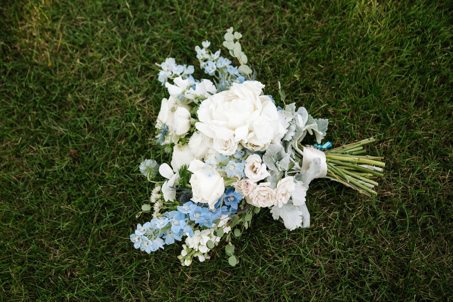 White and blue floral wedding bouquet arrangements laid out on green grass.