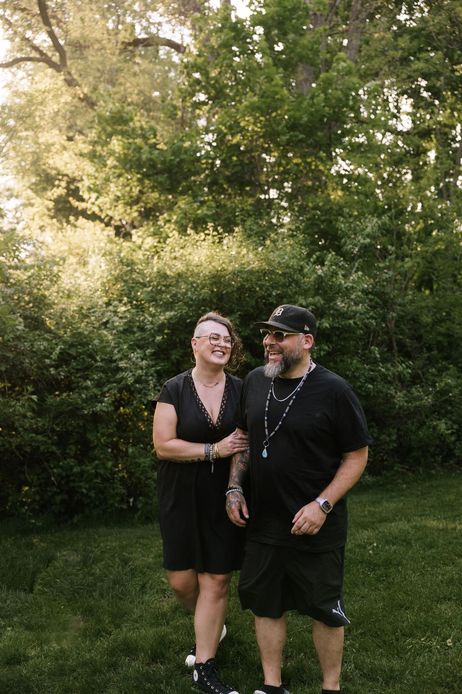 Couple in black outfits laughing together in green garden setting.