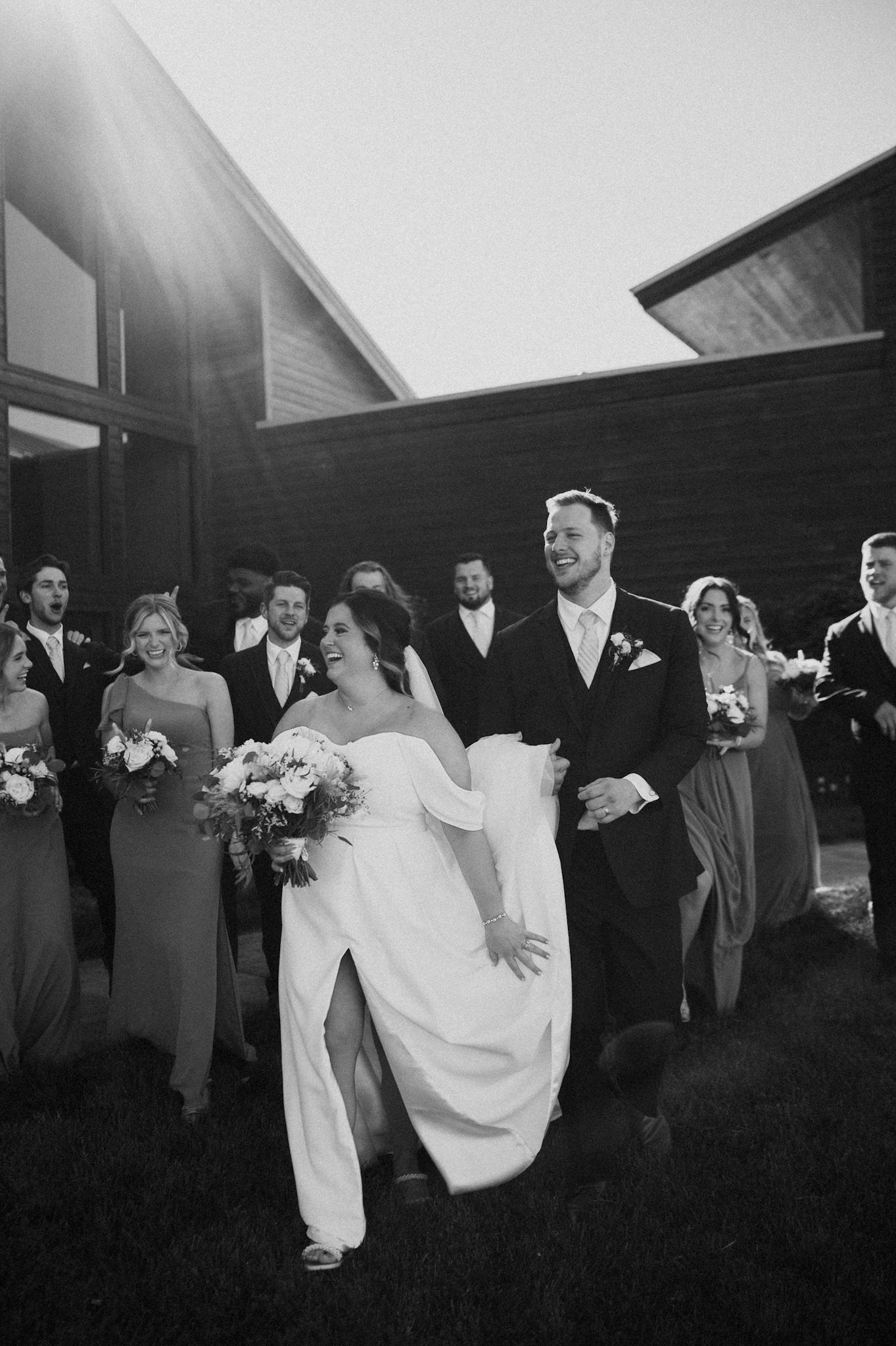 Wedding party lined up outside rustic buildings in black and white.