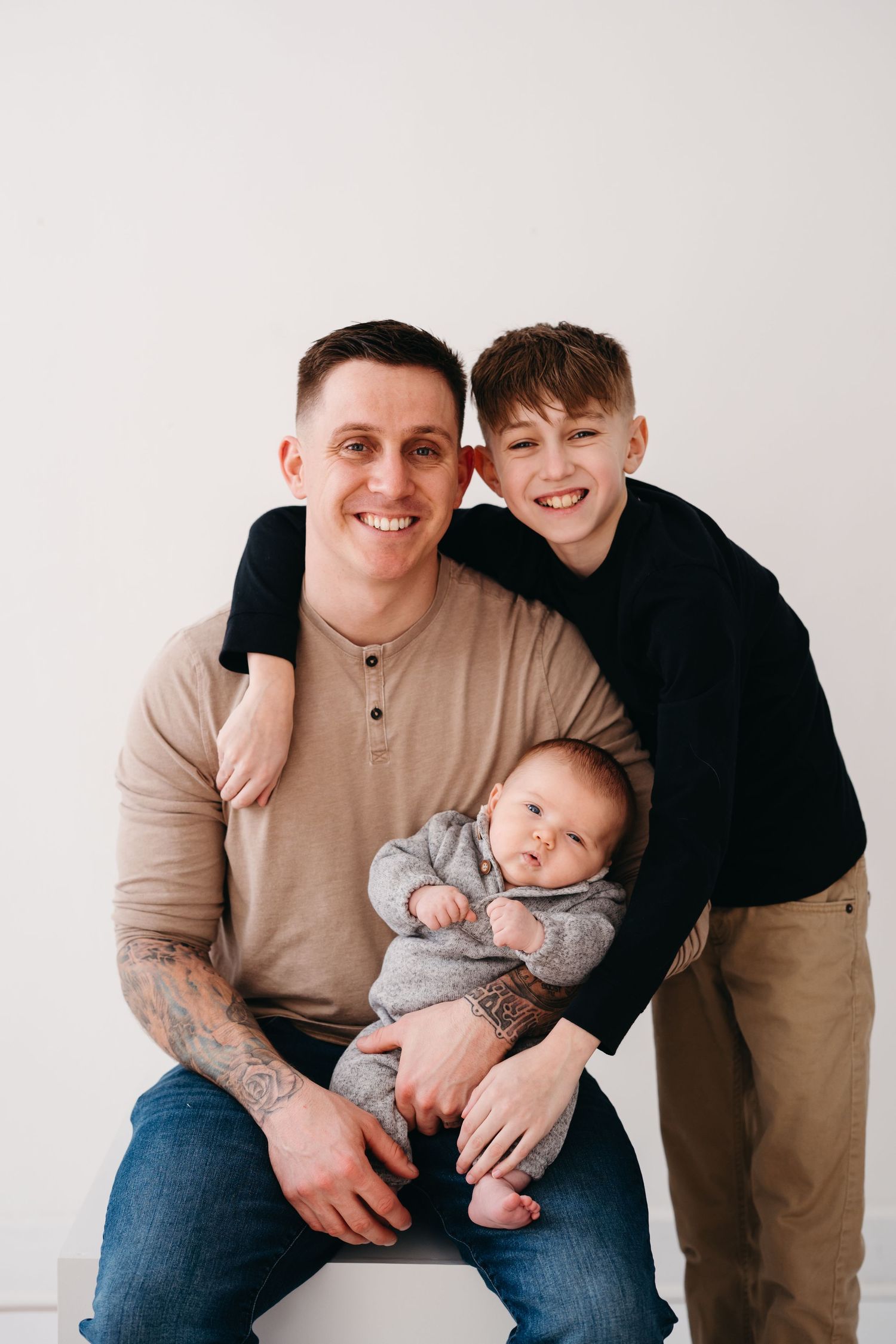 A casual indoor family portrait featuring three people against a minimal white background.