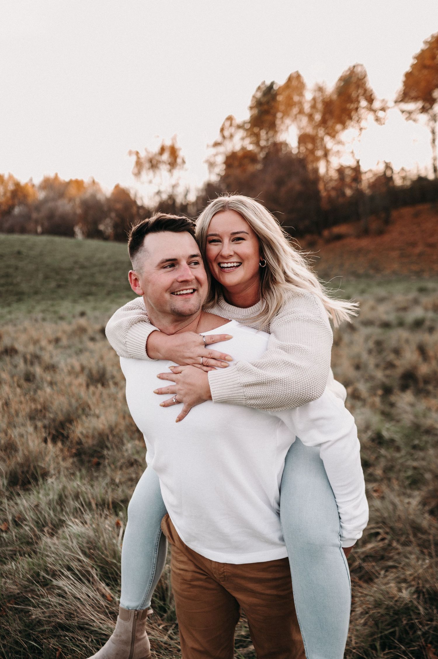 Joyful couple sharing laughter during piggyback ride in autumn field.