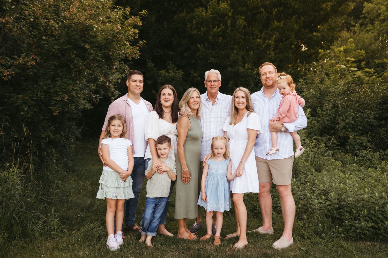 Extended family portrait outdoors with multiple generations wearing coordinated white and neutral outfits.