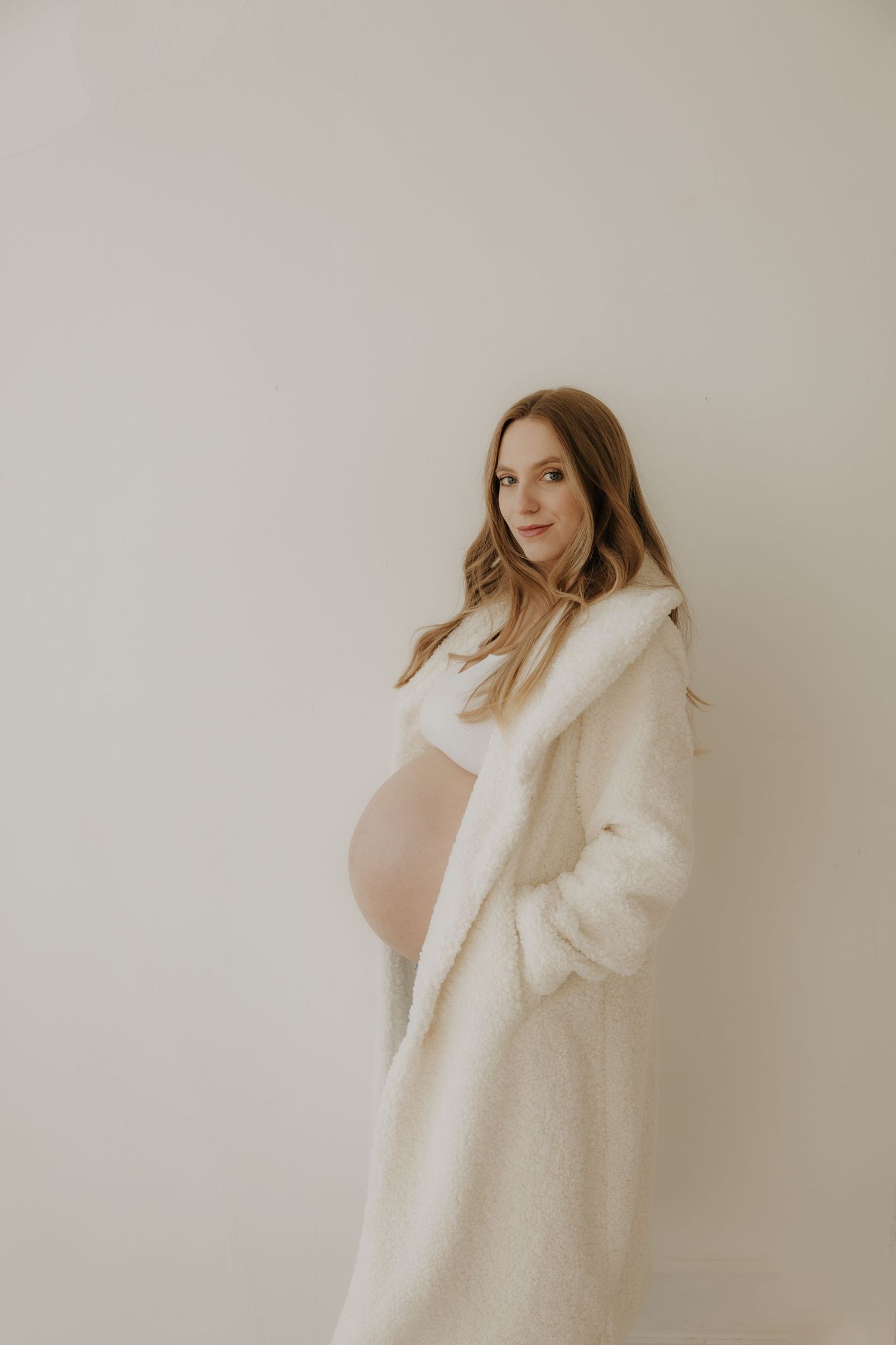 Minimalist maternity portrait with woman wearing cozy white cardigan.