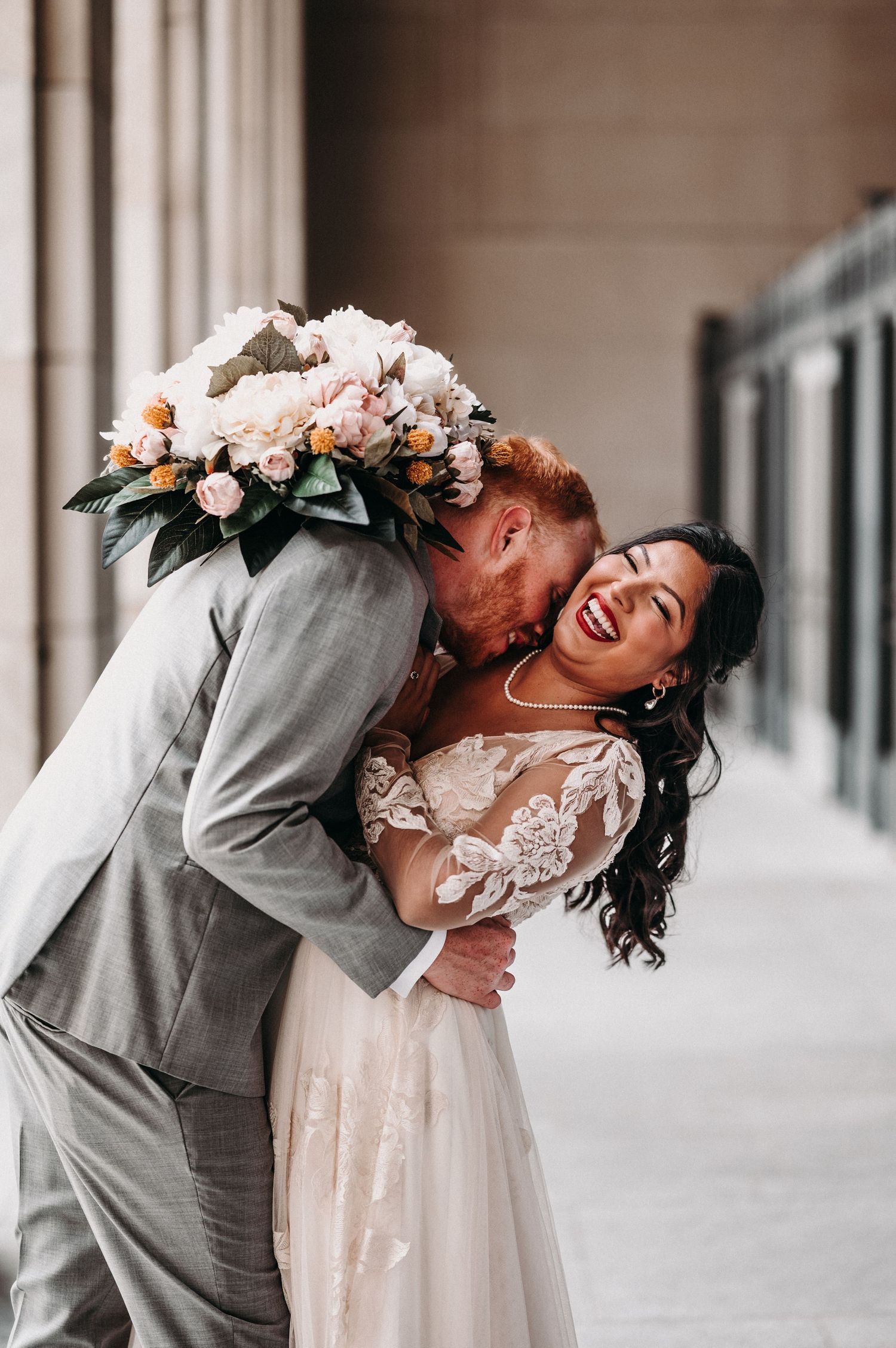 A joyful wedding moment captured showing laughter and love in front of stone architecture.