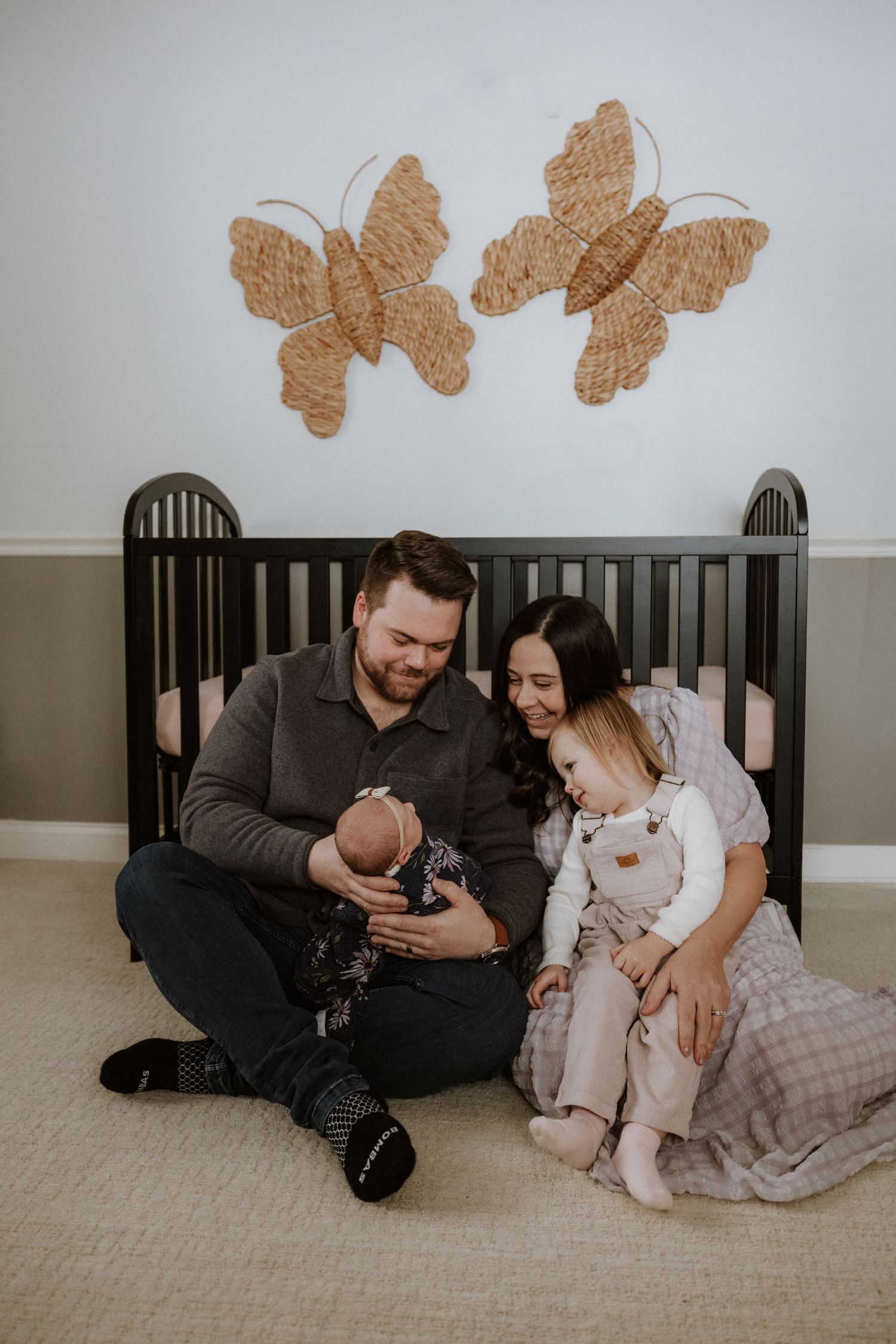 Family sitting together on floor with baby and decorative butterflies on wall in nursery.