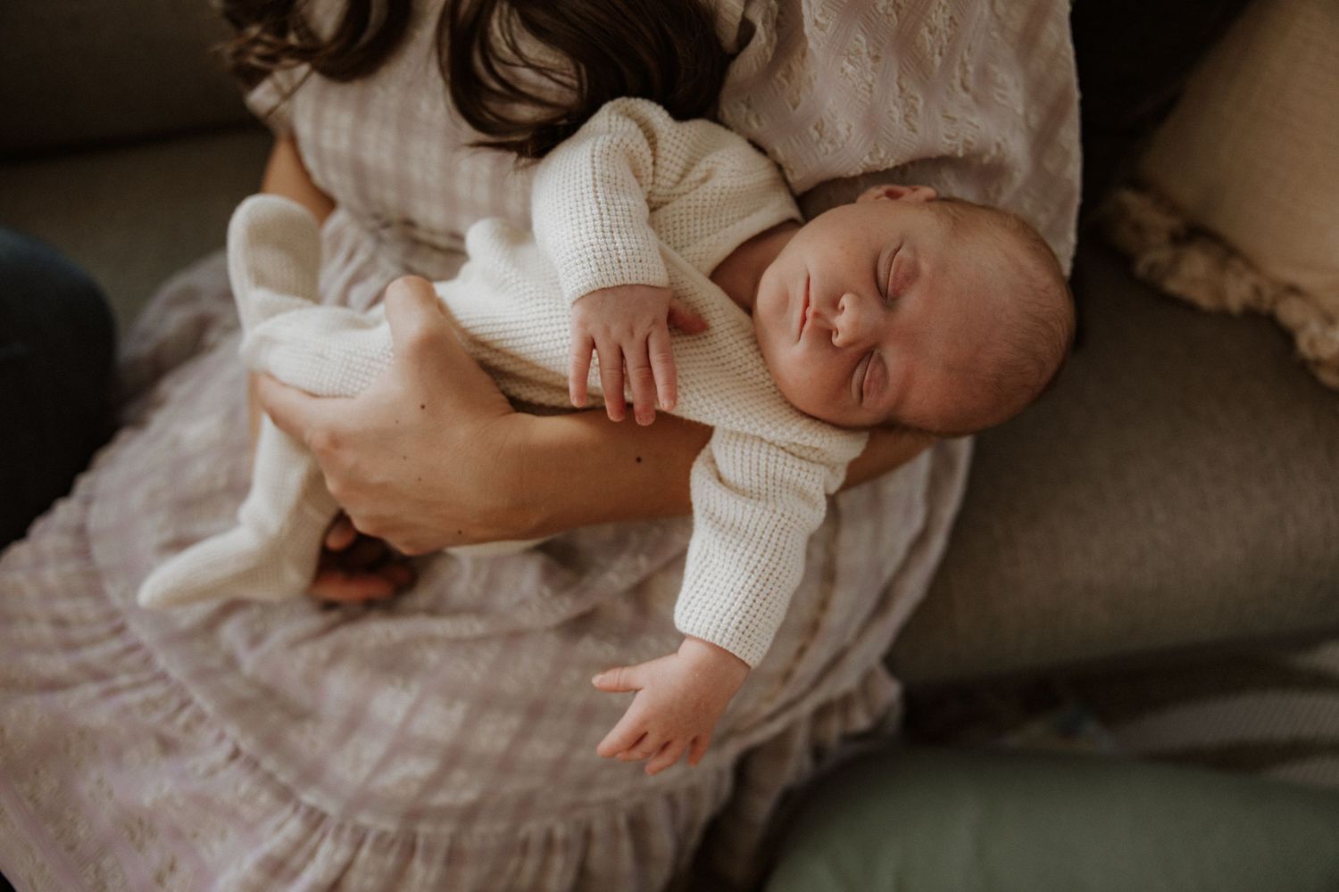 Baby in white clothing being held tenderly in natural window light.