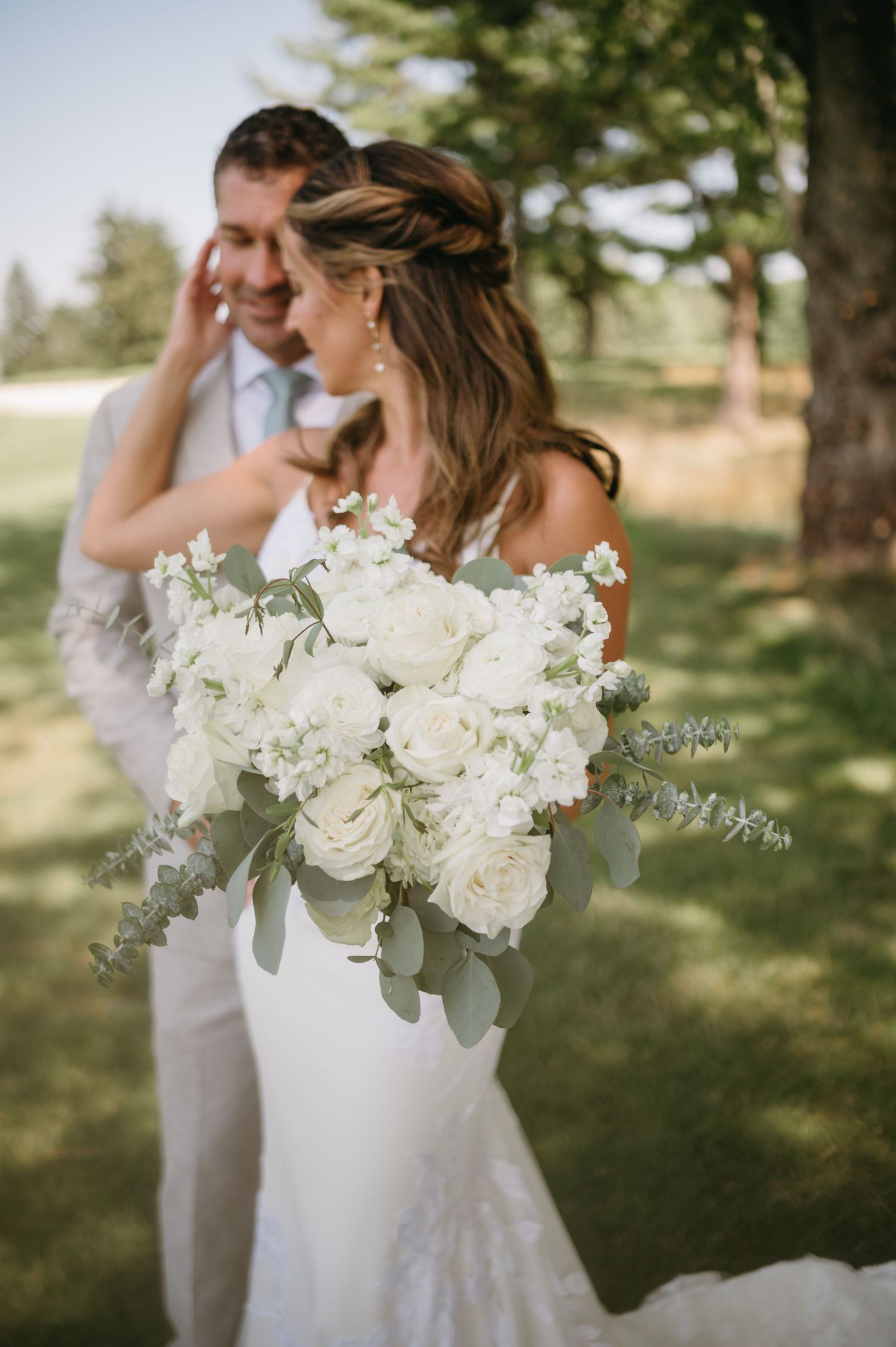Elegant white floral bouquet with roses and greenery against an outdoor garden setting.