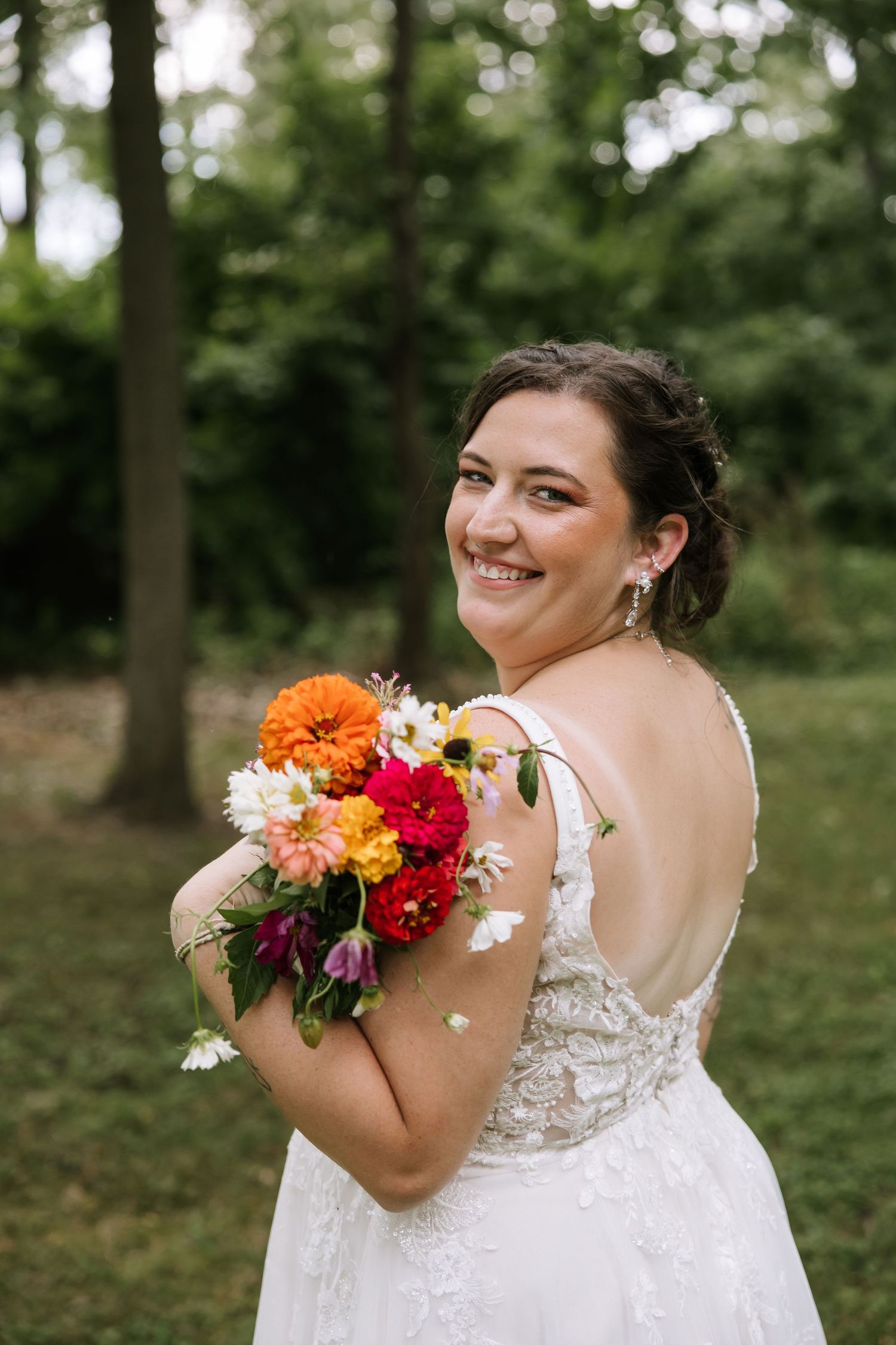 A bride in a white lace dress holds a vibrant bouquet of orange and red flowers.