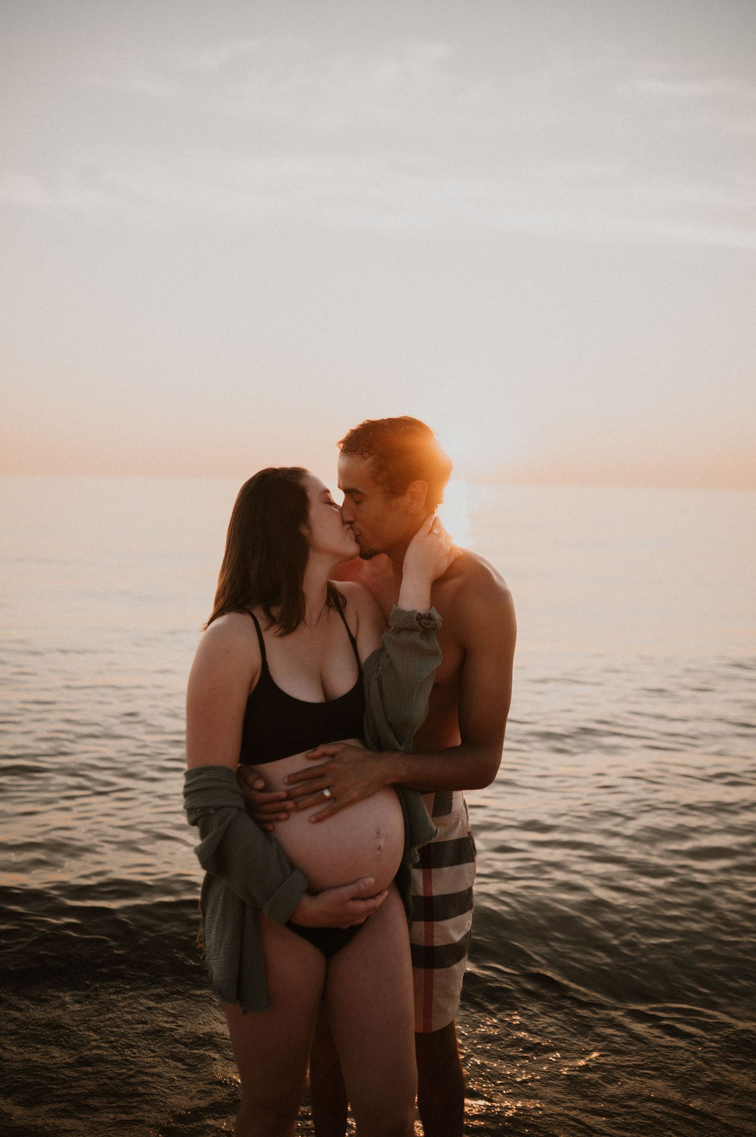 Romantic maternity photo of couple embracing on beach during golden hour.