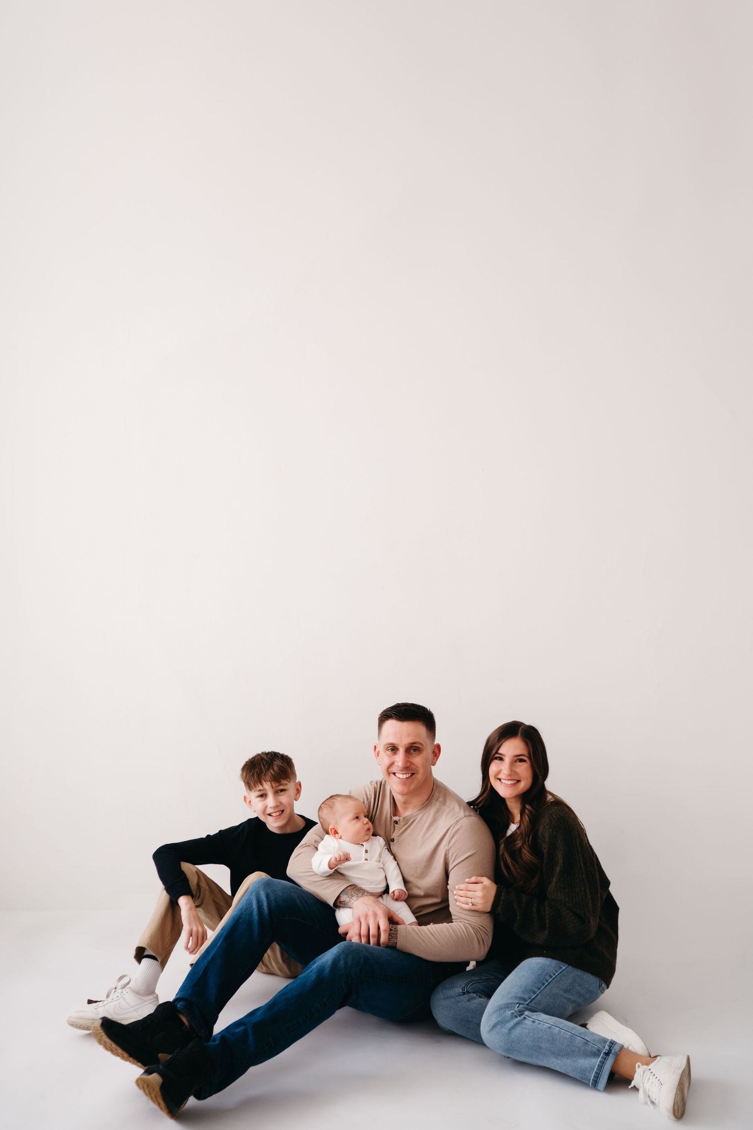 Family sitting together on white floor during indoor portrait session with newborn baby.