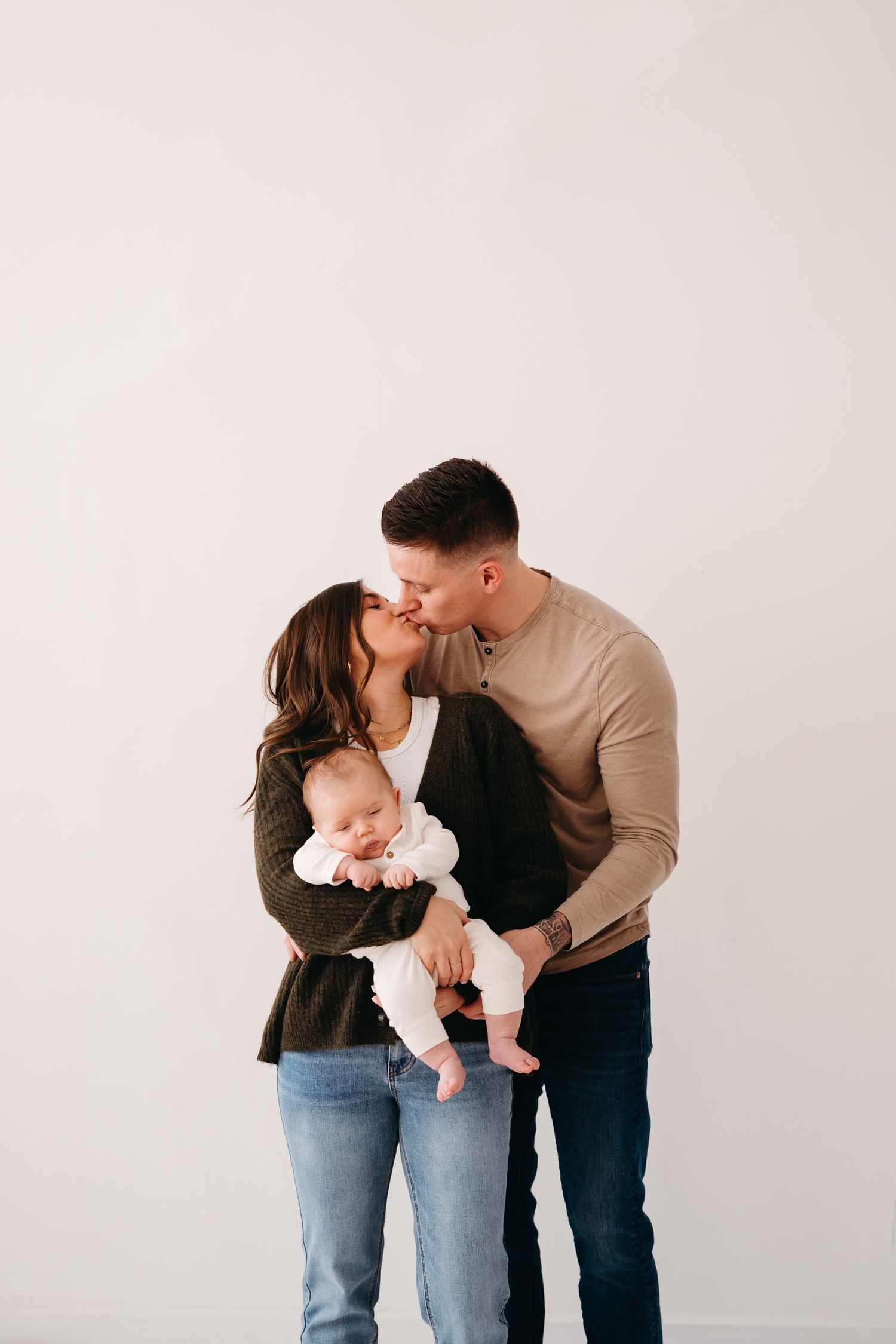 Family sharing intimate moment with baby against plain white wall.