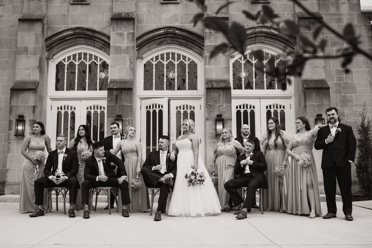 Black and white portrait of full wedding party lined up against church exterior.