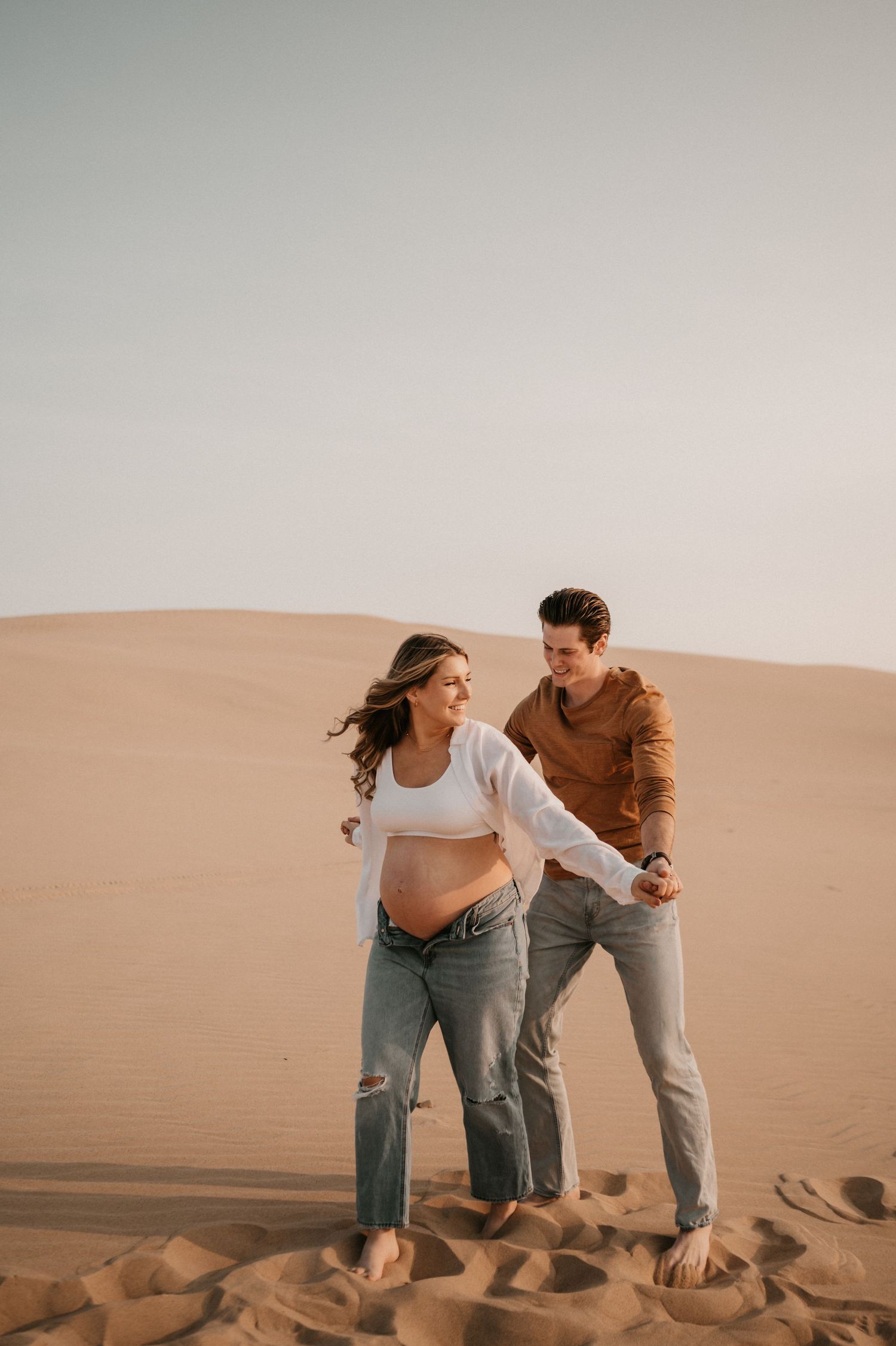A couple shares a romantic moment on sand dunes during golden hour.