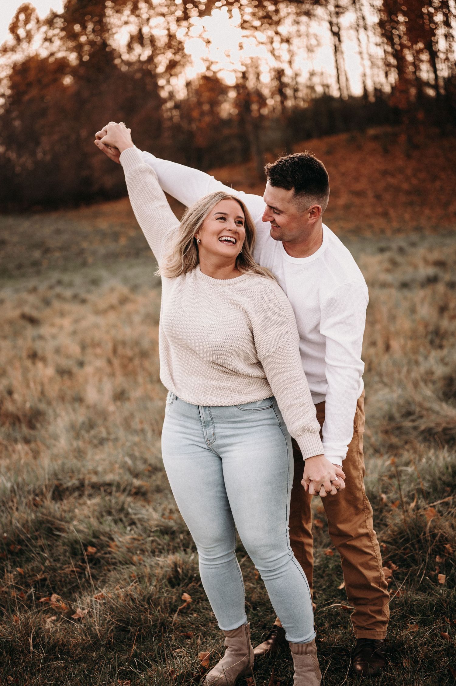 Dancing couple in casual sweaters enjoying autumn sunset in field.