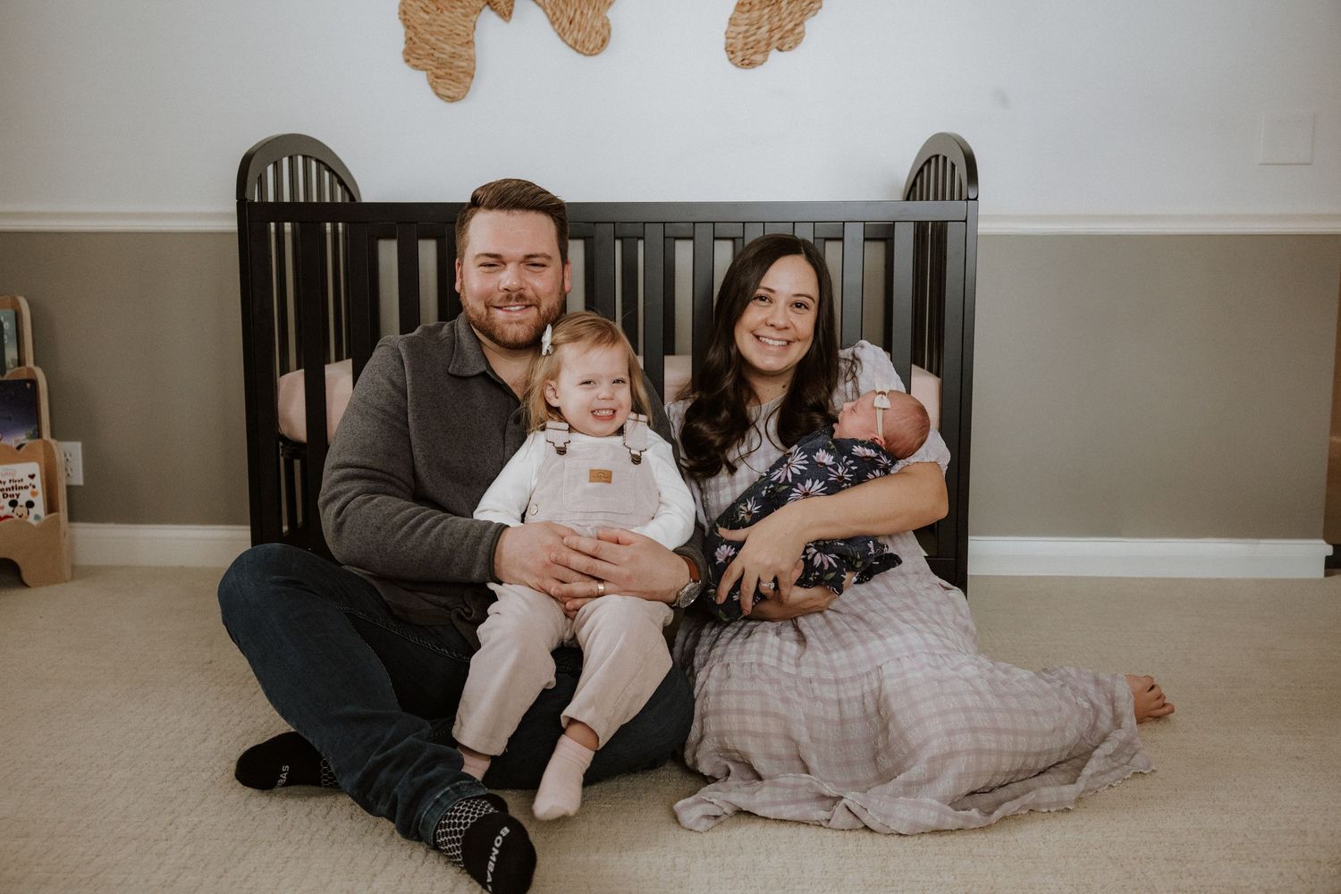 Family gathered on floor by dark crib with butterfly wall decorations above.