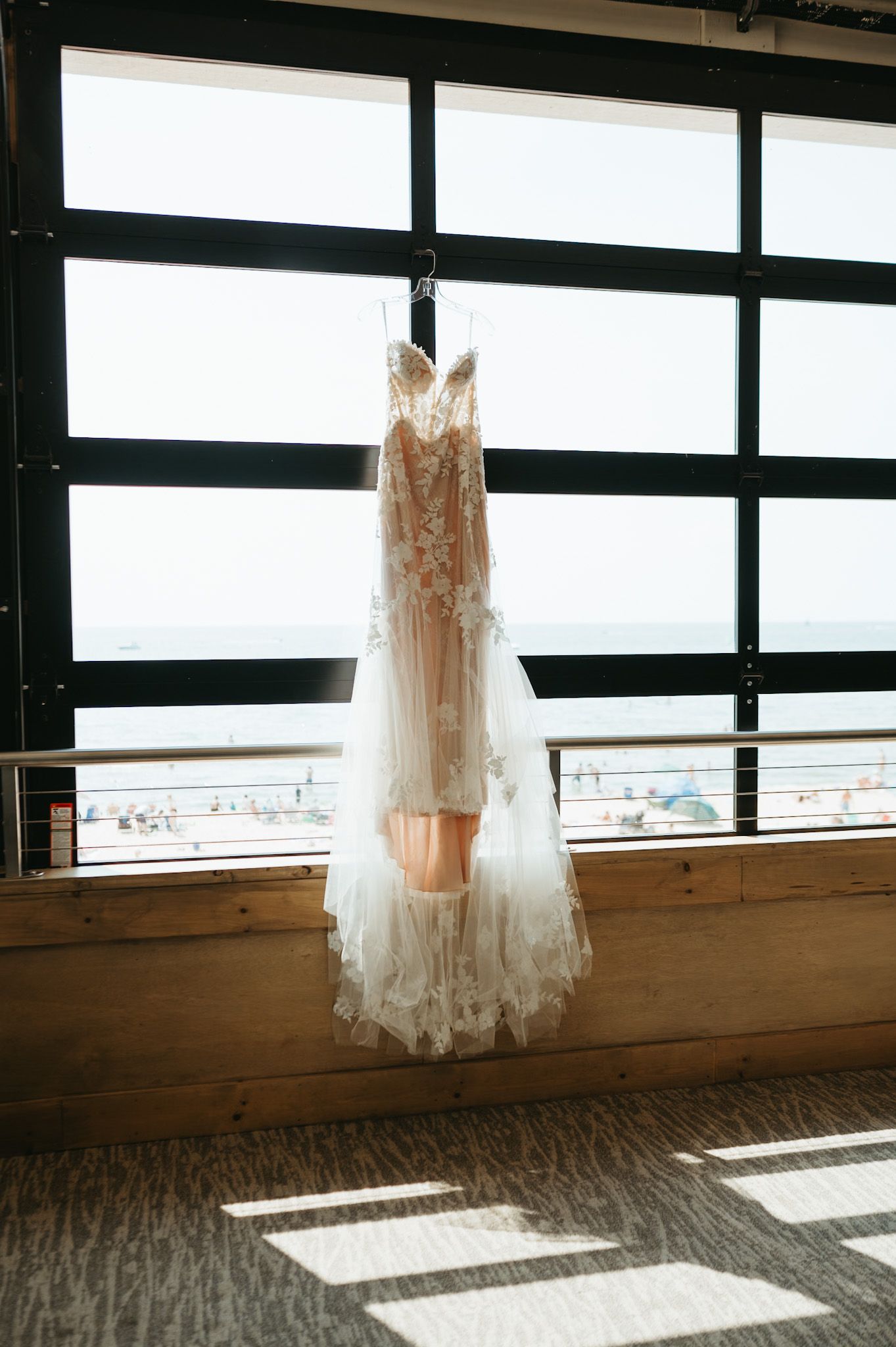 Delicate lace wedding dress hanging in window with natural light streaming through geometric panes.