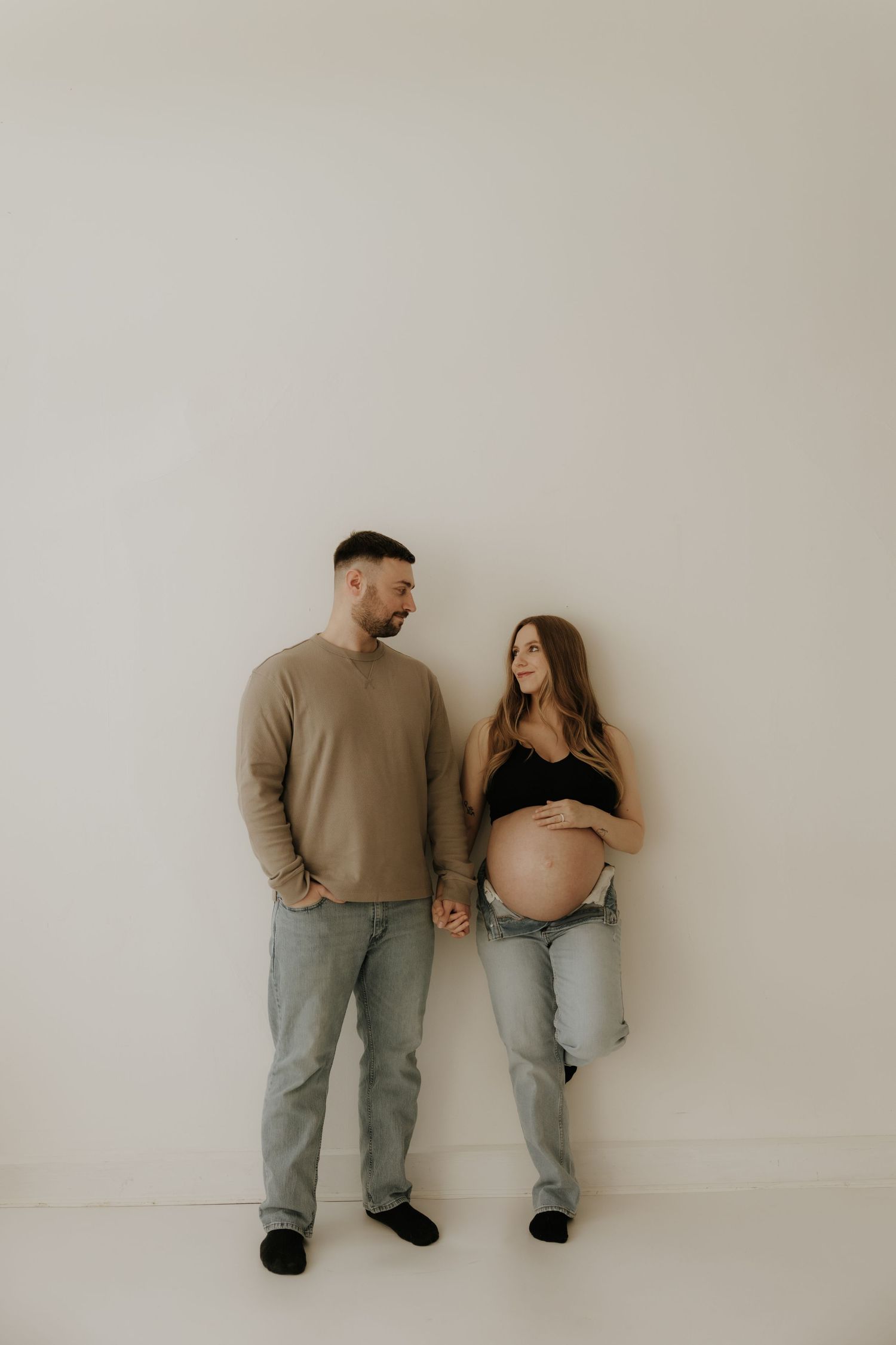 A couple stands together against a white wall sharing an intimate moment.