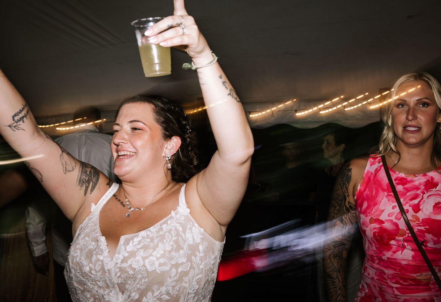 People celebrating and dancing with raised arms at a festive indoor party with string lights.