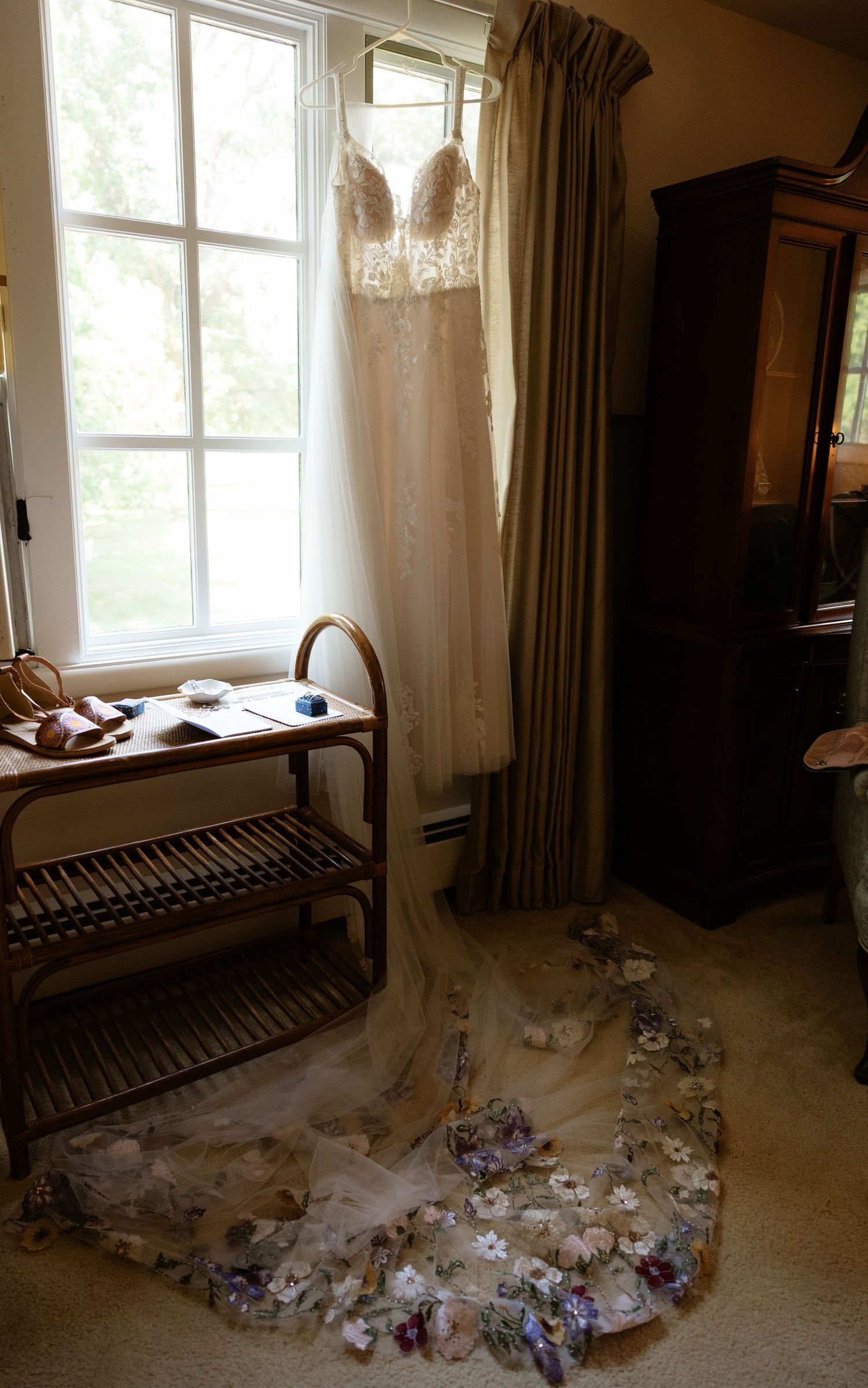 Wedding dress train and veil spread elegantly across a sunlit room with scattered flower petals.