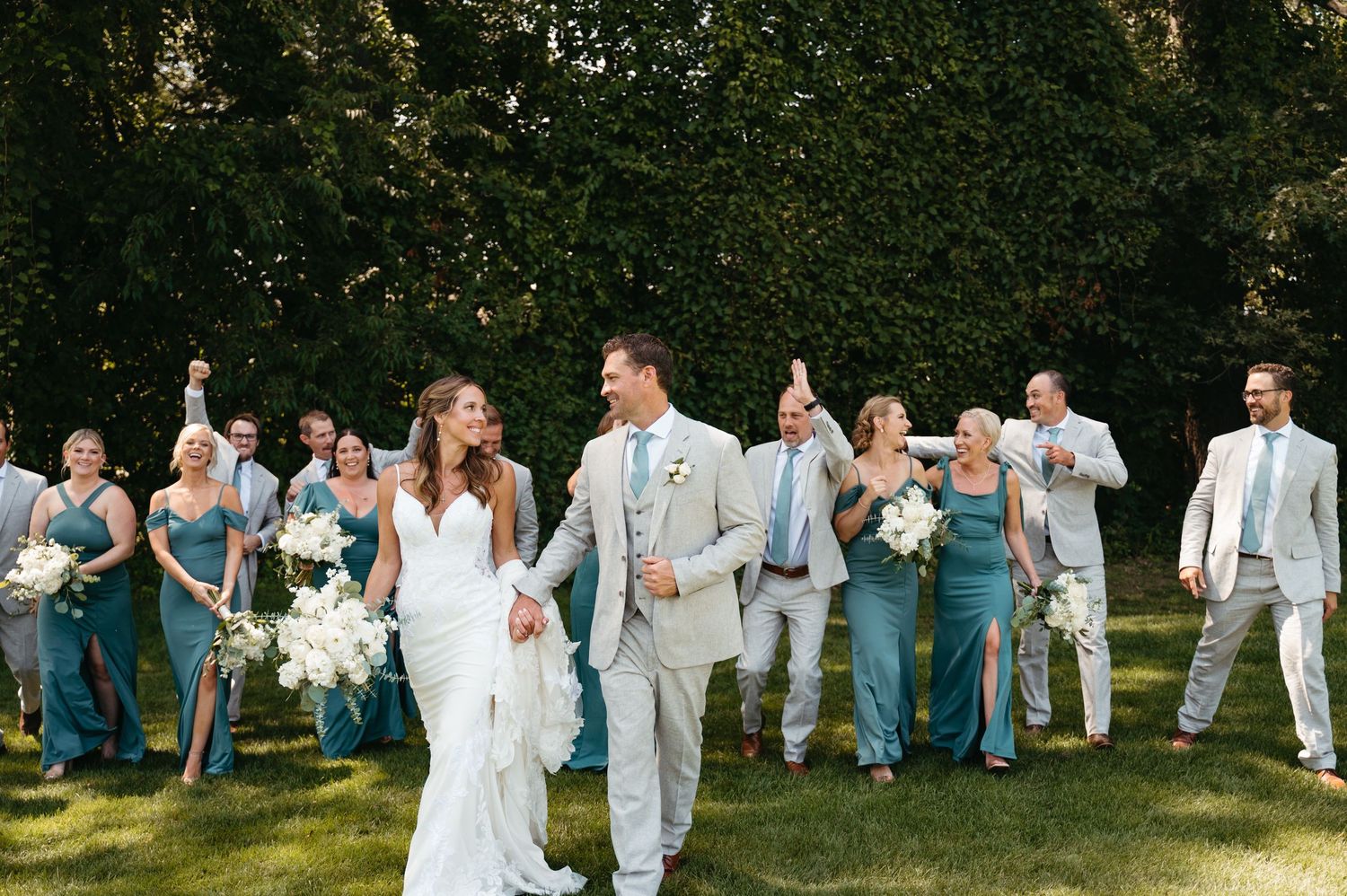 Large wedding party in coordinated blue and grey attire posing outdoors.