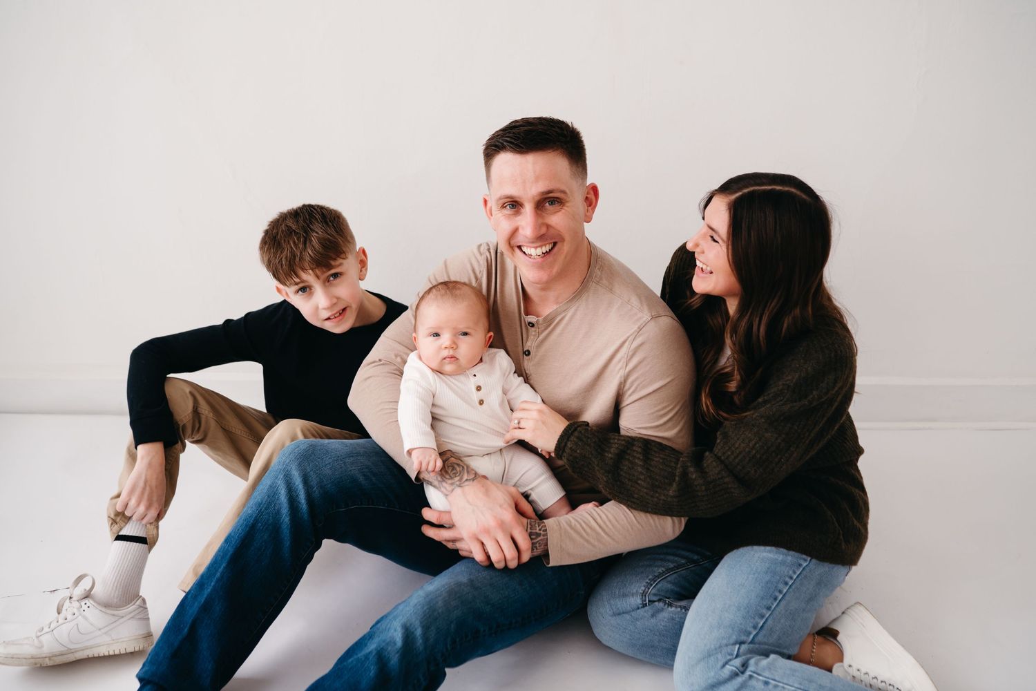 Family sitting together and smiling with baby against white backdrop.