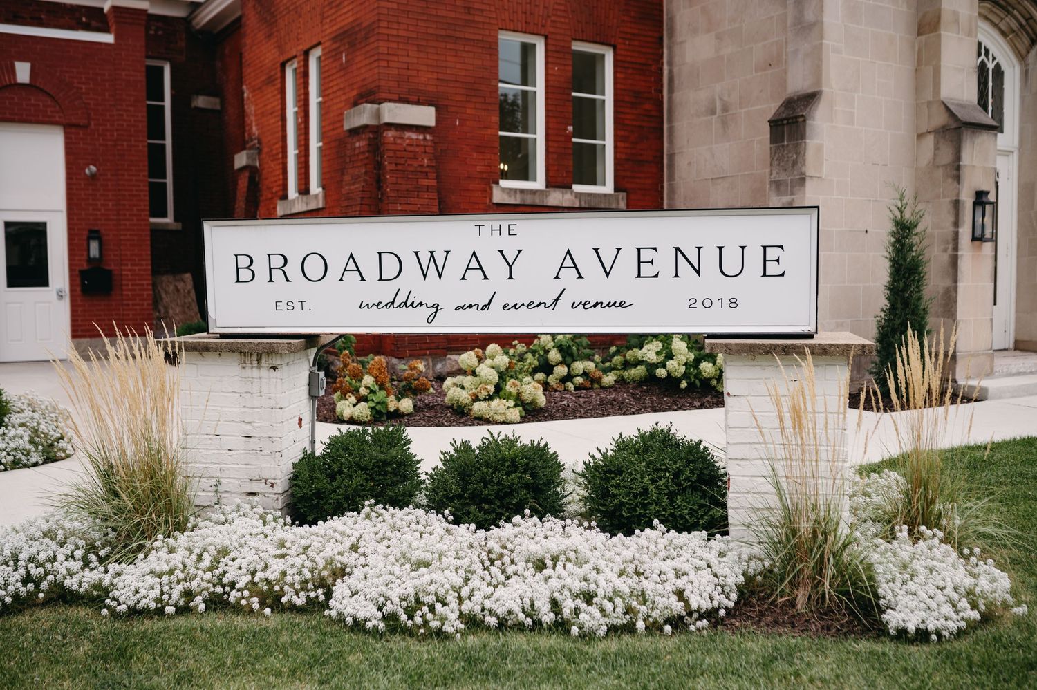 Broadway Avenue church sign surrounded by white flowers and ornamental grasses.