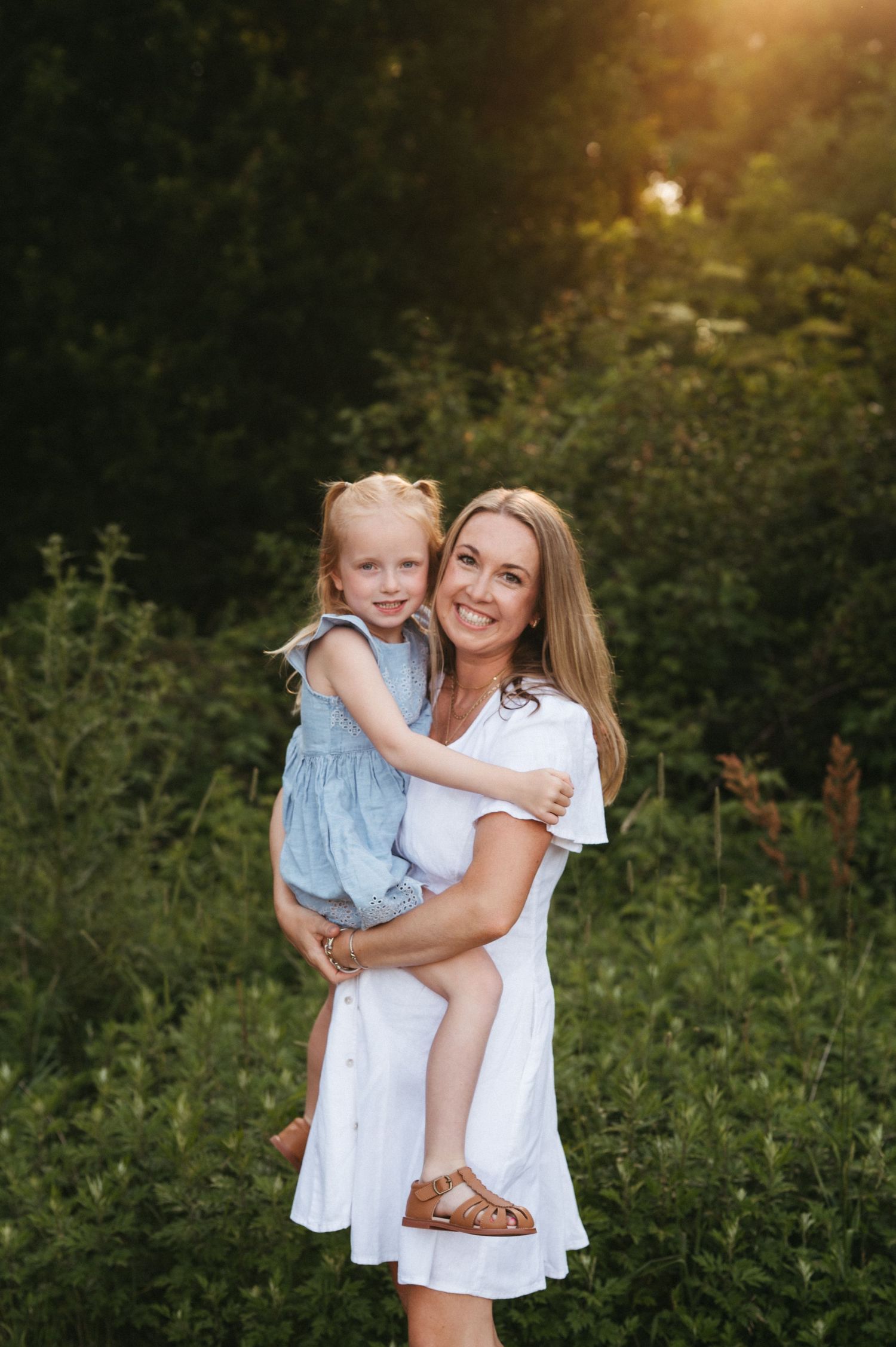A sweet outdoor portrait in a white dress against a sunset-lit forest backdrop.