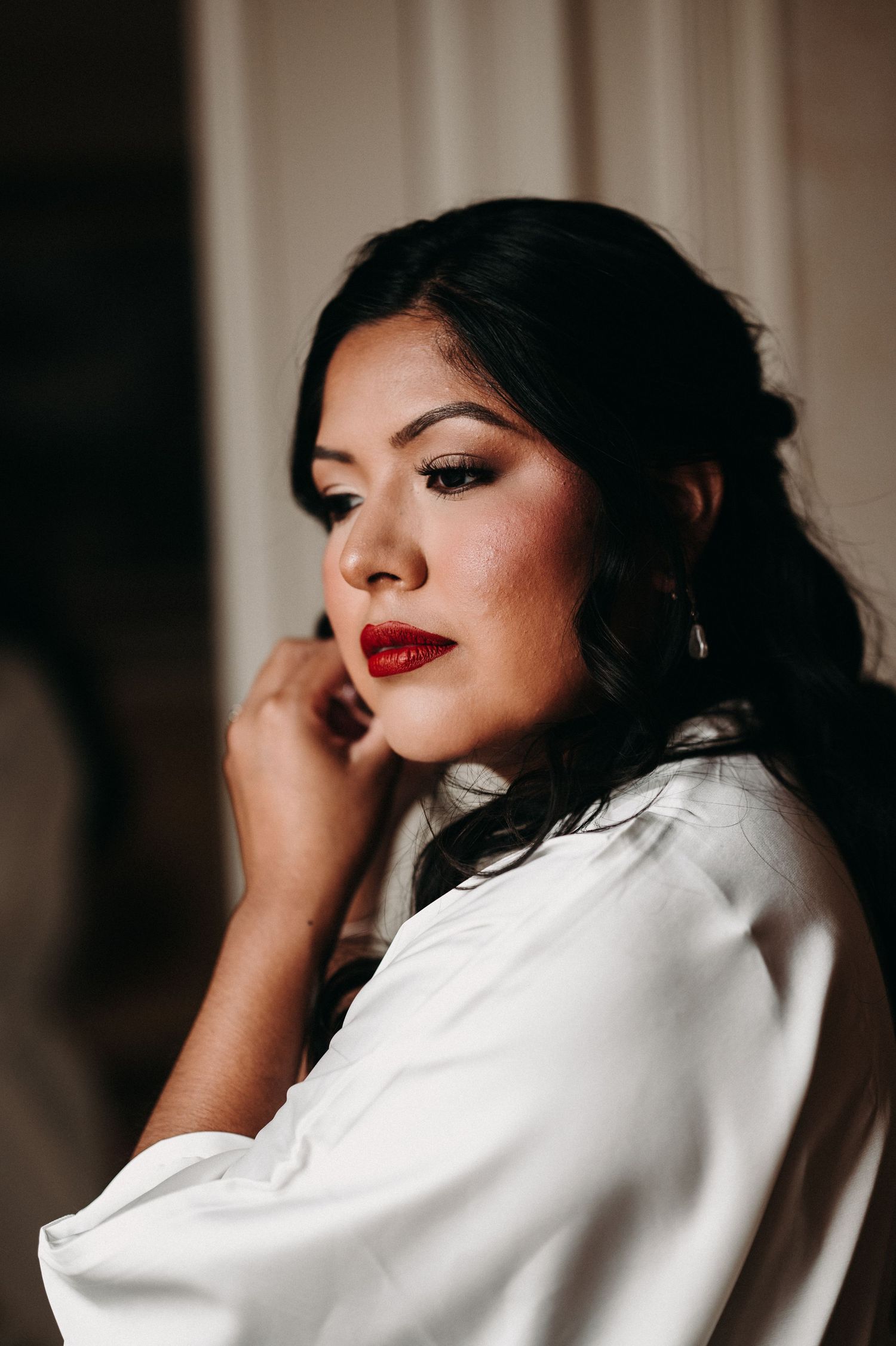 A portrait in moody lighting shows elegant bridal makeup and a white robe.