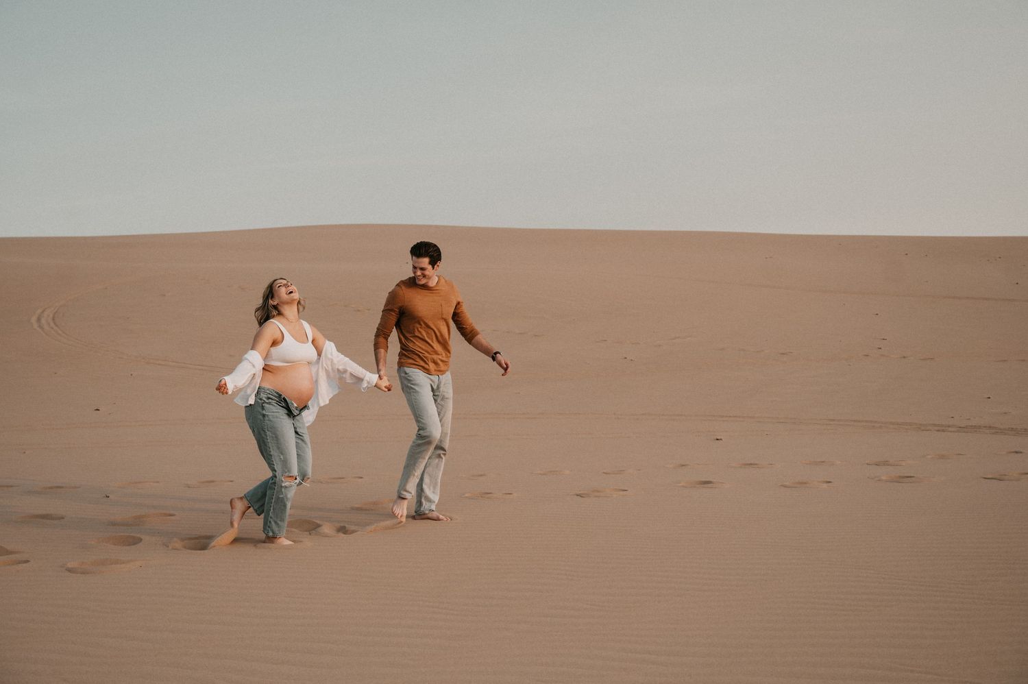 Two people stroll together across a vast desert landscape at dusk.