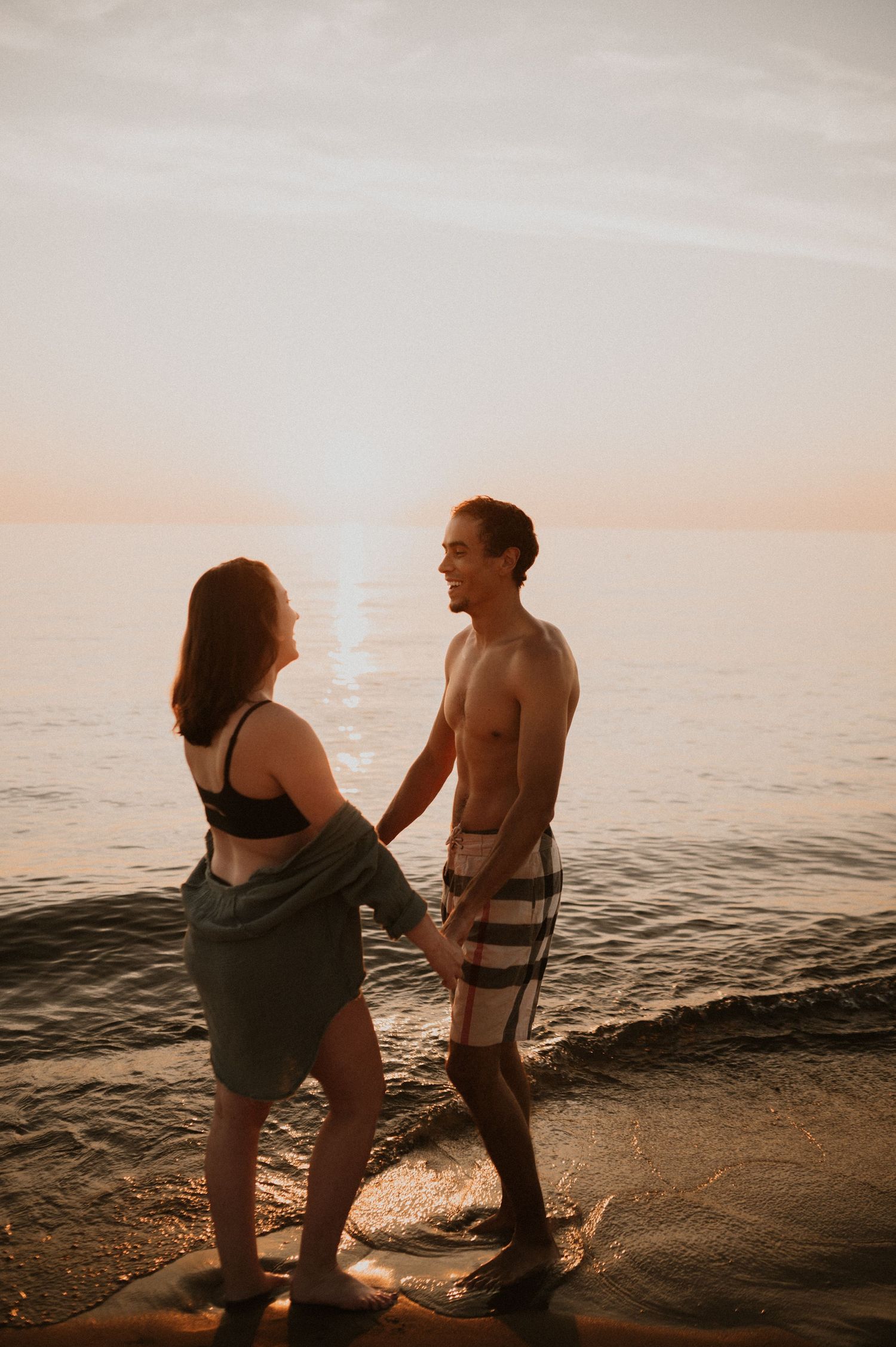 Intimate couple moment on beach at sunset with ocean waves in background.