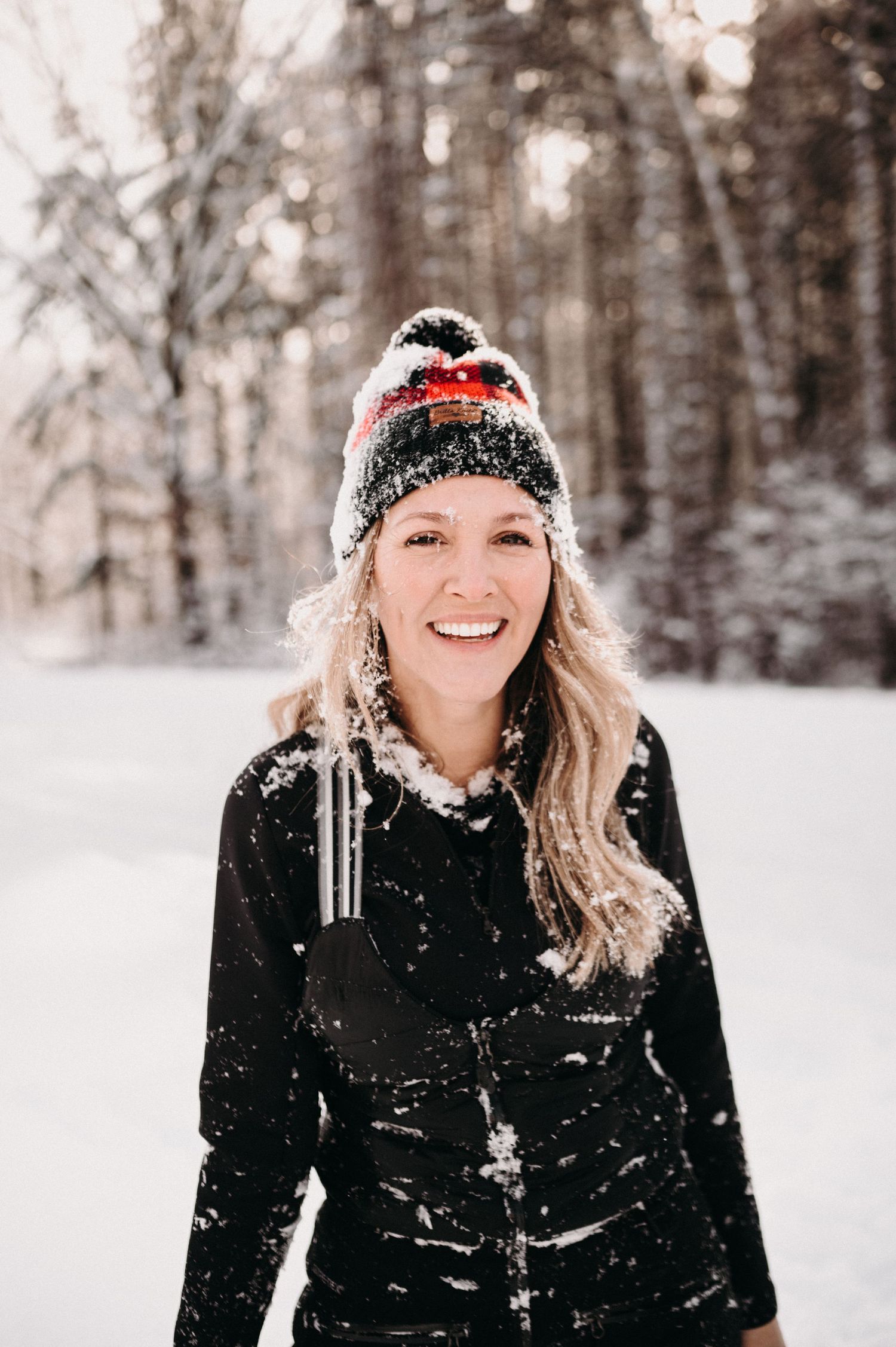 Winter adventurer wearing a knit beanie and black jacket in a snow-covered forest.