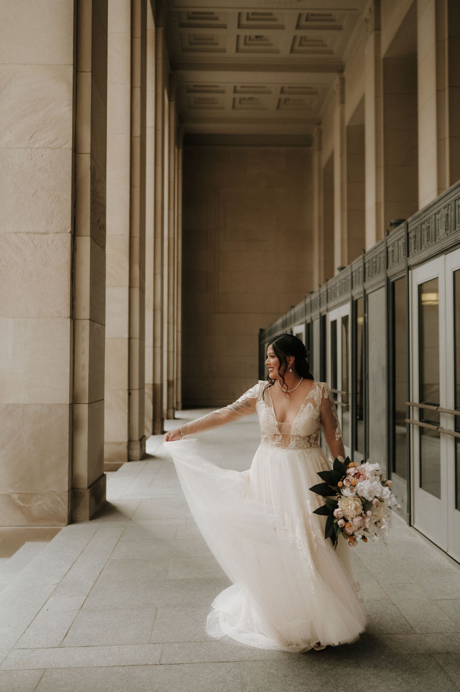 Bride twirls in flowing white gown in elegant colonnade with classical architecture.