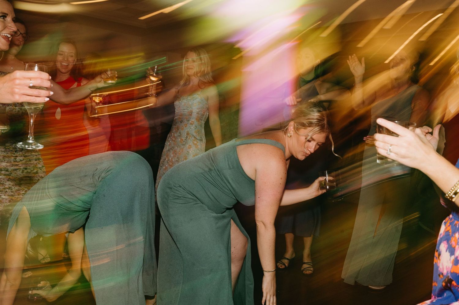 Motion-blurred photo of wedding guests dancing with colorful lights in the background.
